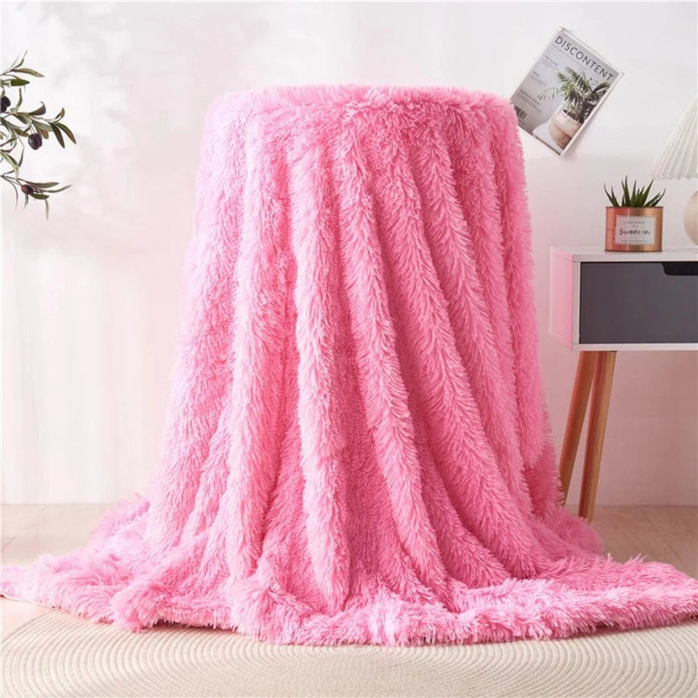 A blush pink luxury faux fur blanket with a textured plush design, elegantly draped over a wooden floor.