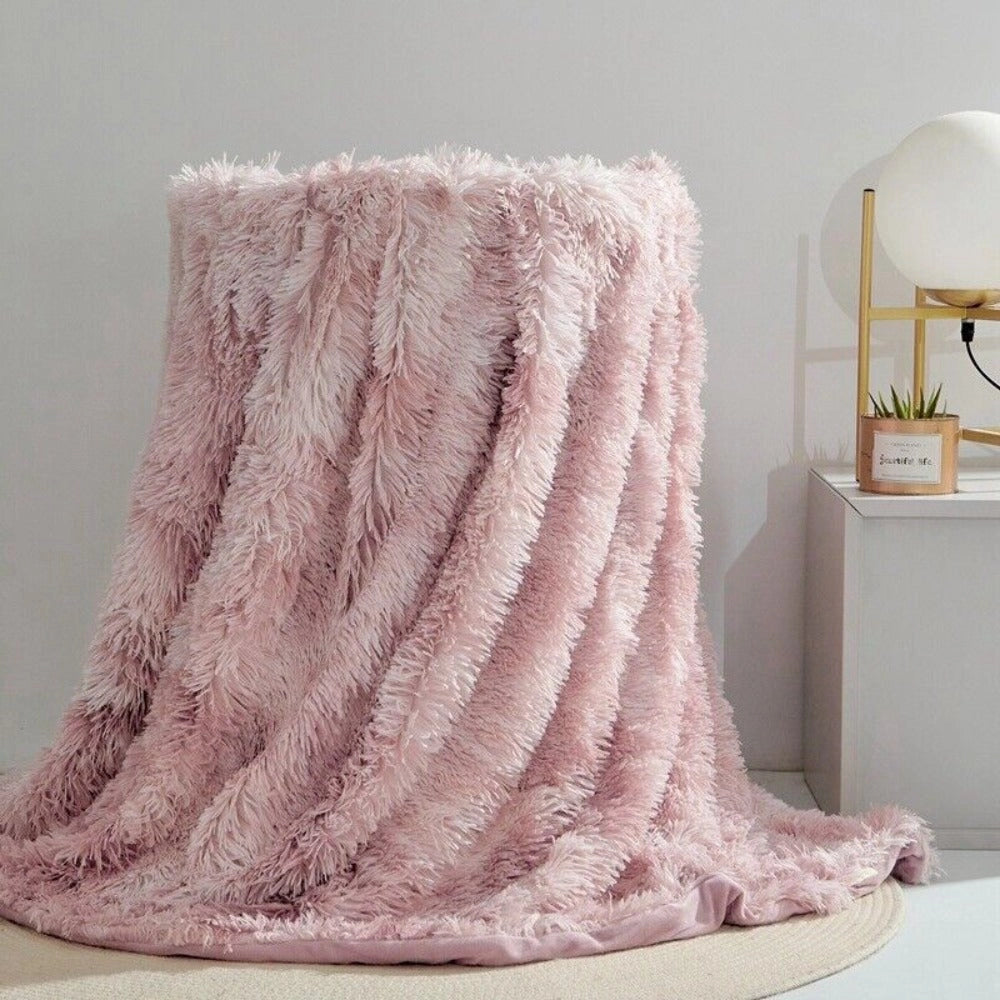 Luxurious white faux fur blanket with a textured and plush design, displayed in a blossom pink color variant. The blanket is elegantly draped on a wooden surface, showcasing its cozy and stylish appearance. The large size of 200x300cm is ideal for adding warmth and elegance to any space.