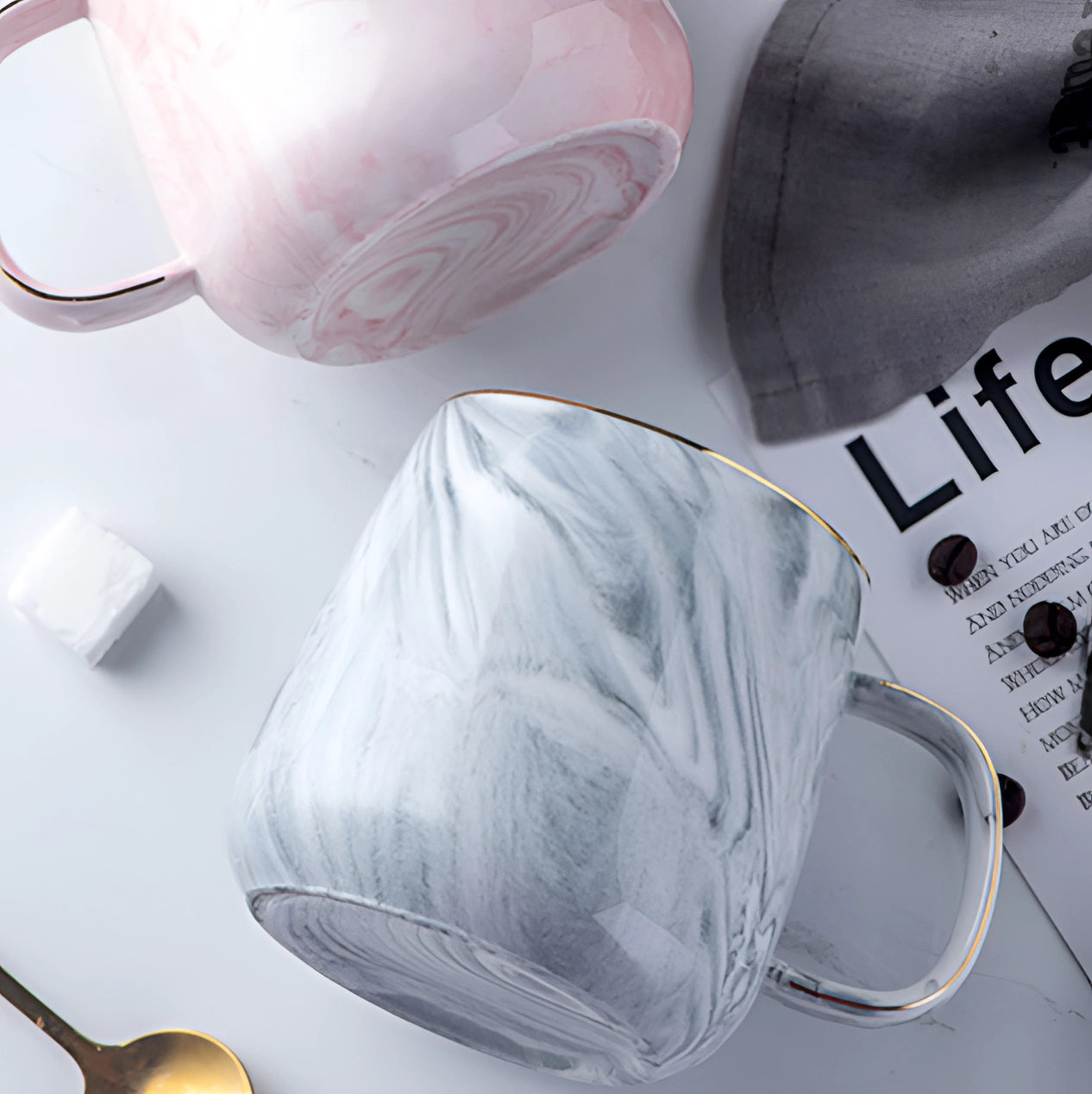 A marble coffee mug with a metallic handle, featuring a blend of pink, grey, and white colors.