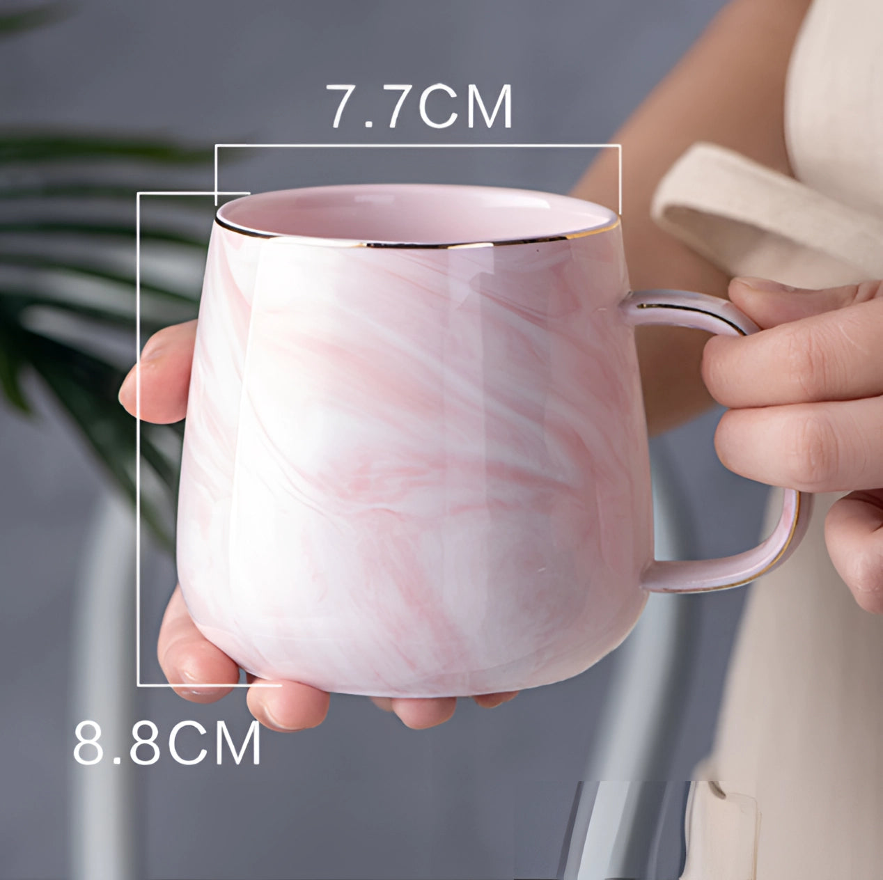 A hand holding a marble coffee mug with a metallic handle, featuring a pink, grey, and white marbled design.