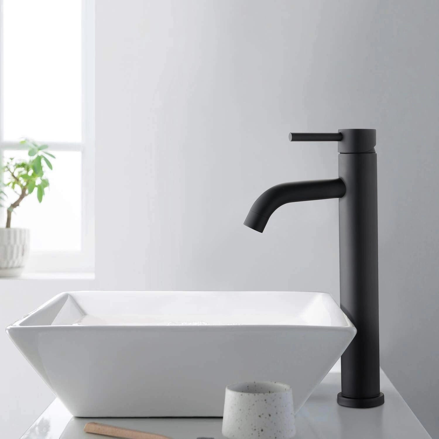 Sleek matte black modern bathroom faucet with minimalist design, mounted on a wooden sink counter, accompanied by a potted houseplant, enhancing the contemporary interior aesthetics.