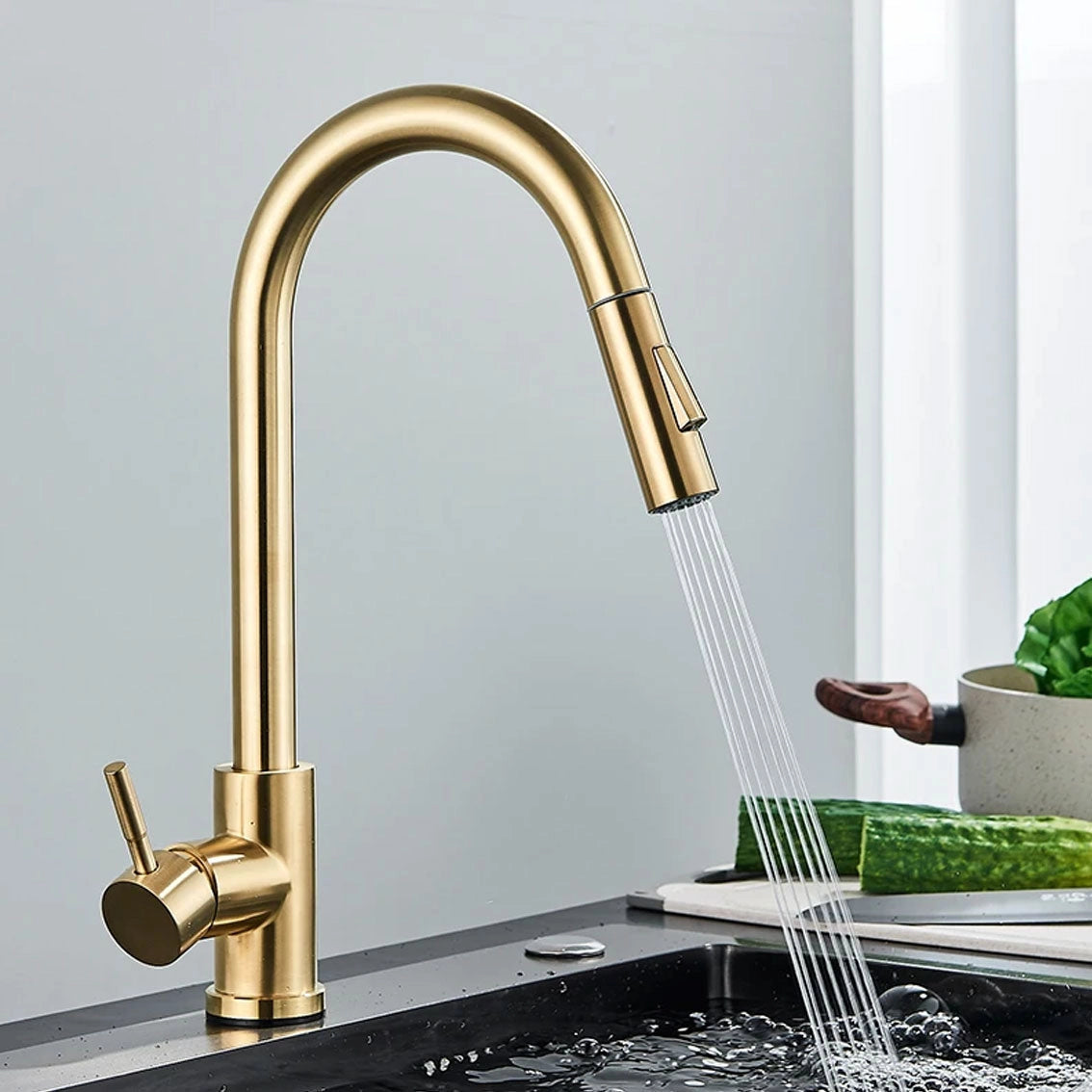 Matte black pull-down kitchen faucet with 360° swivel spout, shown in gold finish, installed on a kitchen sink with surrounding greenery.