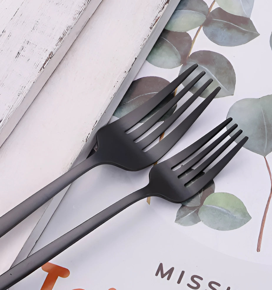 Matte black stainless steel cutlery set featuring a sleek and modern design, including a fork, displayed alongside a white plate on a dining table.