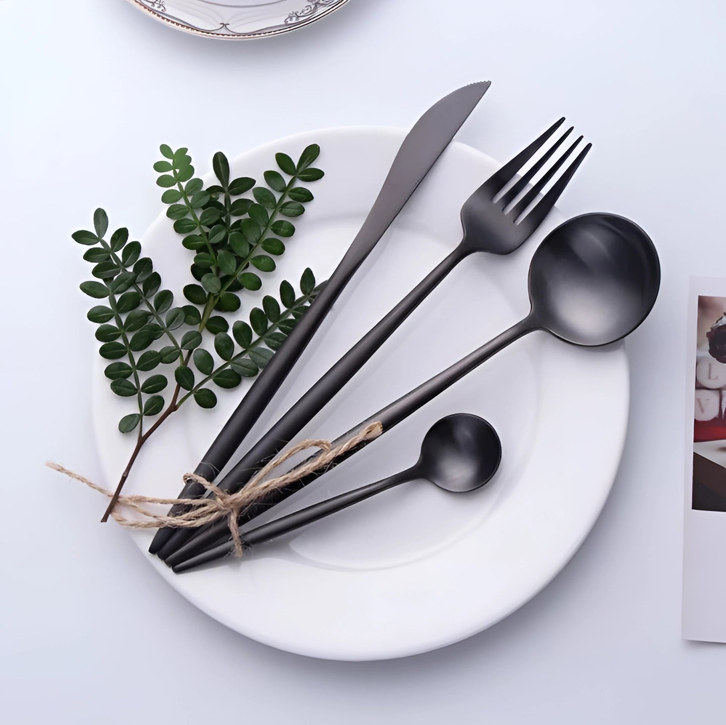 Matte black stainless steel cutlery set displayed on a wooden table, accompanied by a white plate and cloth napkins, showcasing a luxurious and modern table setting.