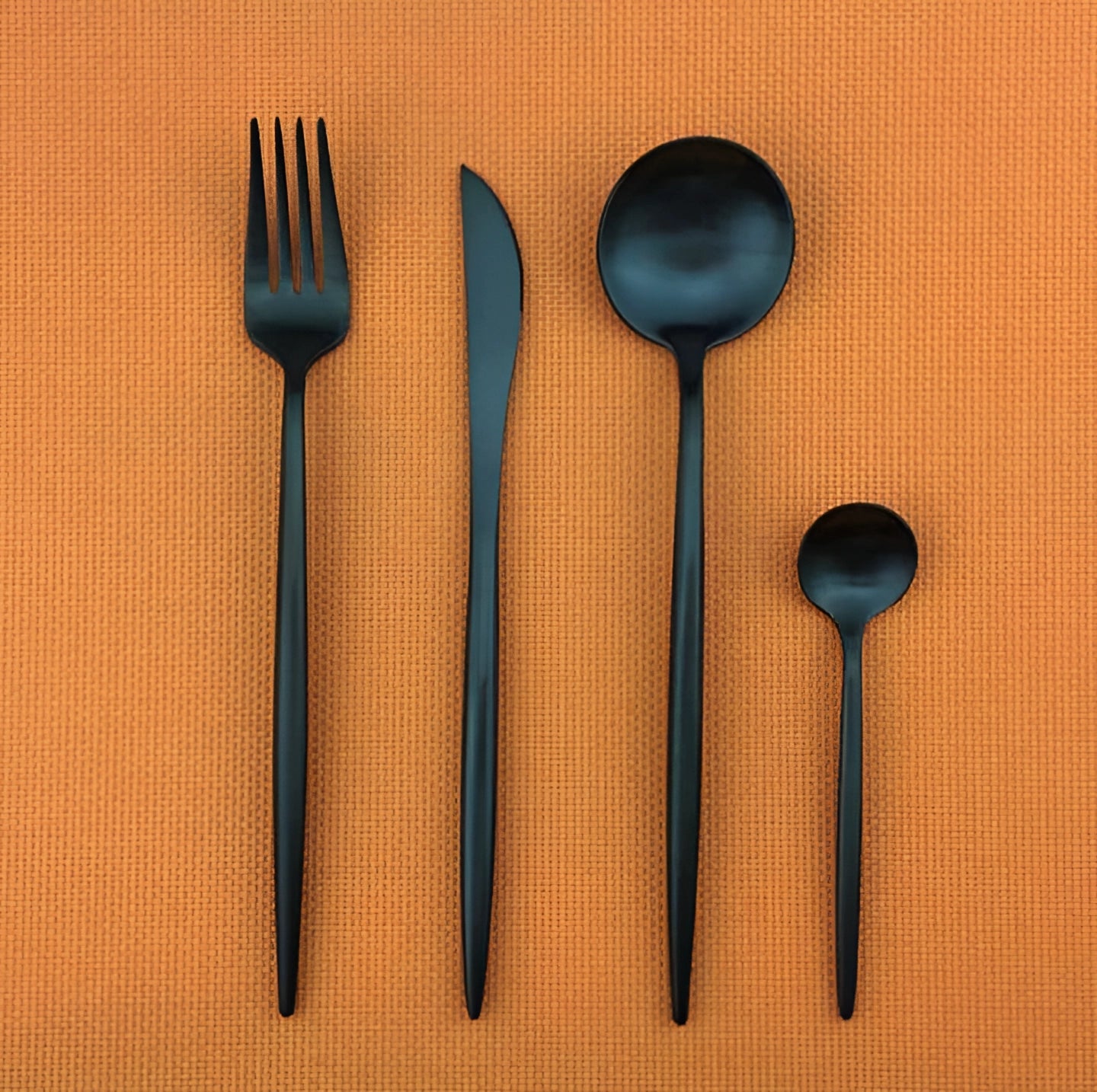 Matte black stainless steel cutlery set including a fork, showcased on a wooden rectangular surface.