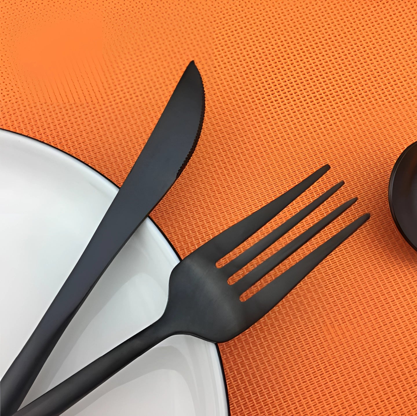 Matte black stainless steel cutlery set including a fork, displayed on an orange background, showcasing luxury designer flatware.