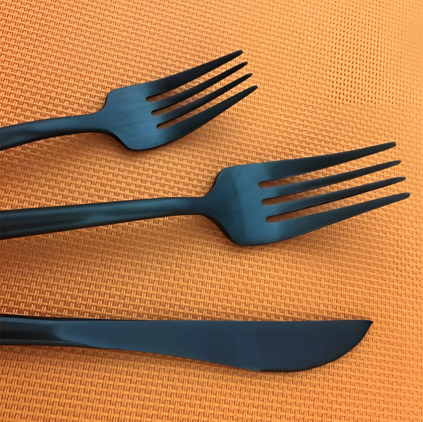 Matte black stainless steel cutlery set displayed on a wooden table, featuring a luxury designer fork and other flatware pieces.