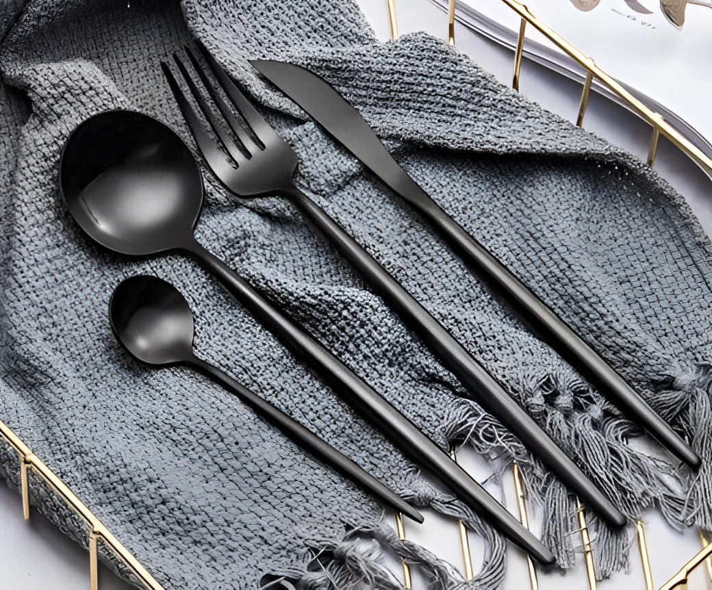 Matte black stainless steel cutlery set consisting of luxury designer flatware, including forks, knives, and spoons, elegantly arranged on a neutral-colored table setting.