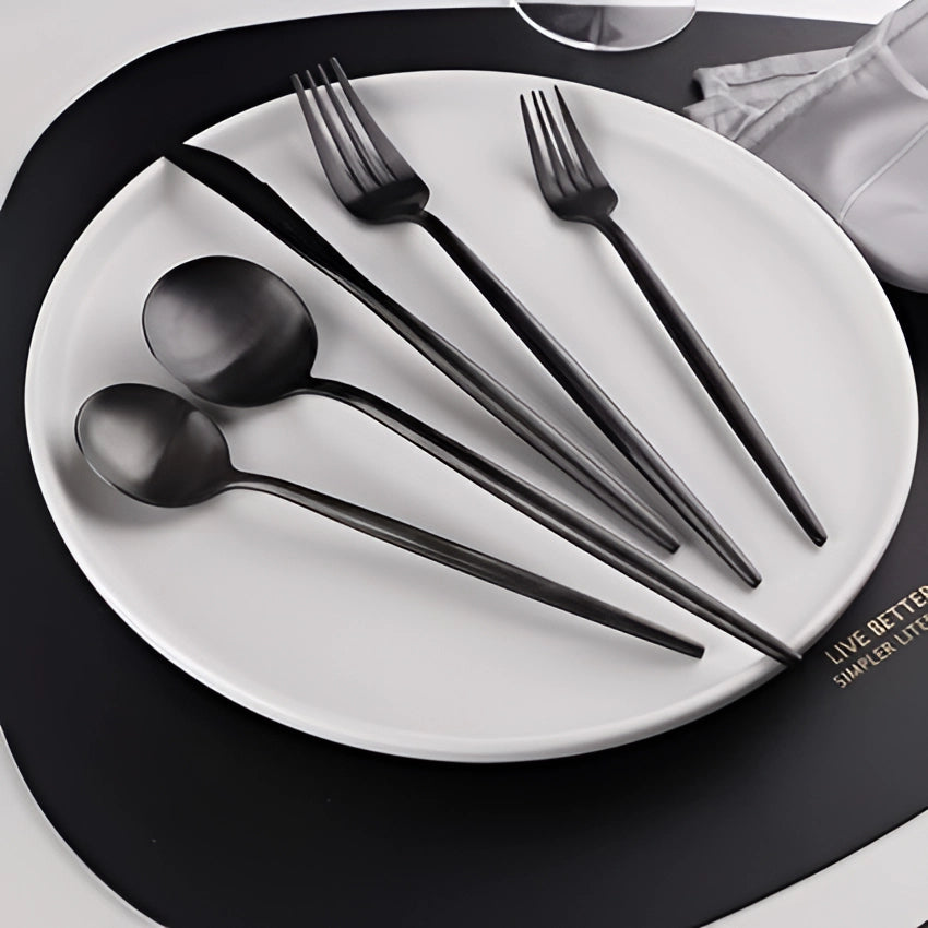 Matte black stainless steel cutlery set featuring a modern minimalist design, displayed on a white plate with a fork, showcasing sleek black and grey kitchen utensils for a contemporary table setting.