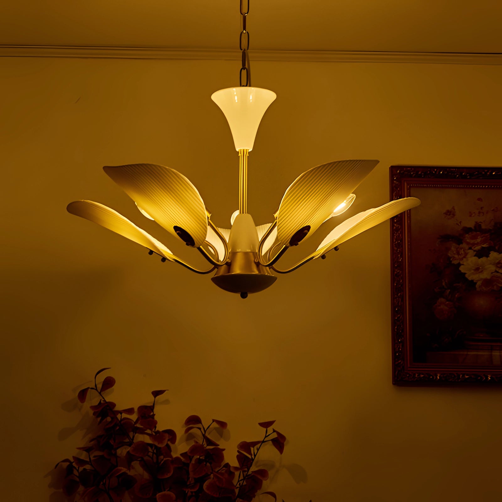 Mid-century modern brass chandelier with white glass shades, featuring a vintage design, hanging in a stylishly decorated interior space with wood accents and plants.