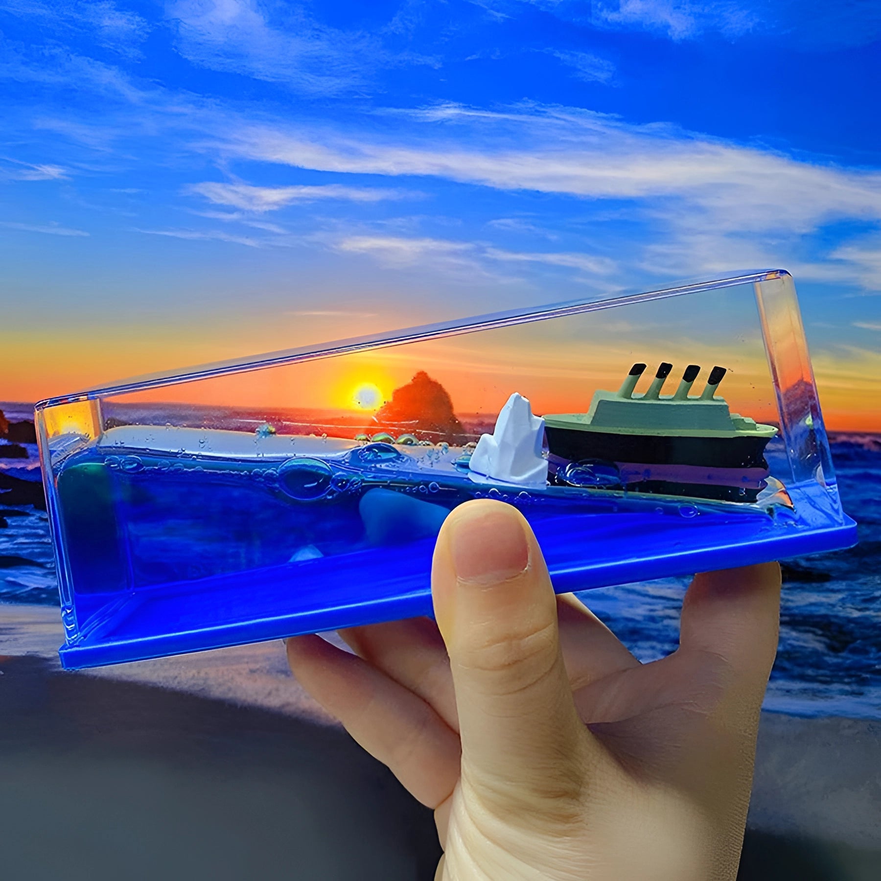 
A miniature model of the Titanic encased in an acrylic wave, set against a serene backdrop of blue sky and water, evoking nautical decor and a sense of travel and leisure.