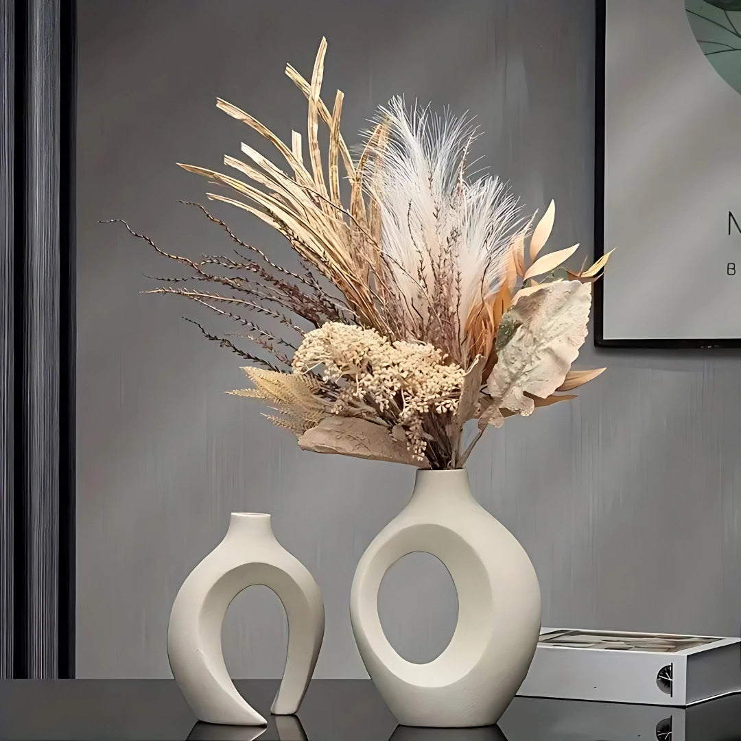 Modern abstract ceramic vase with a smooth white finish, featuring a minimalist design and filled with decorative twigs, placed on a wooden surface in a contemporary setting.