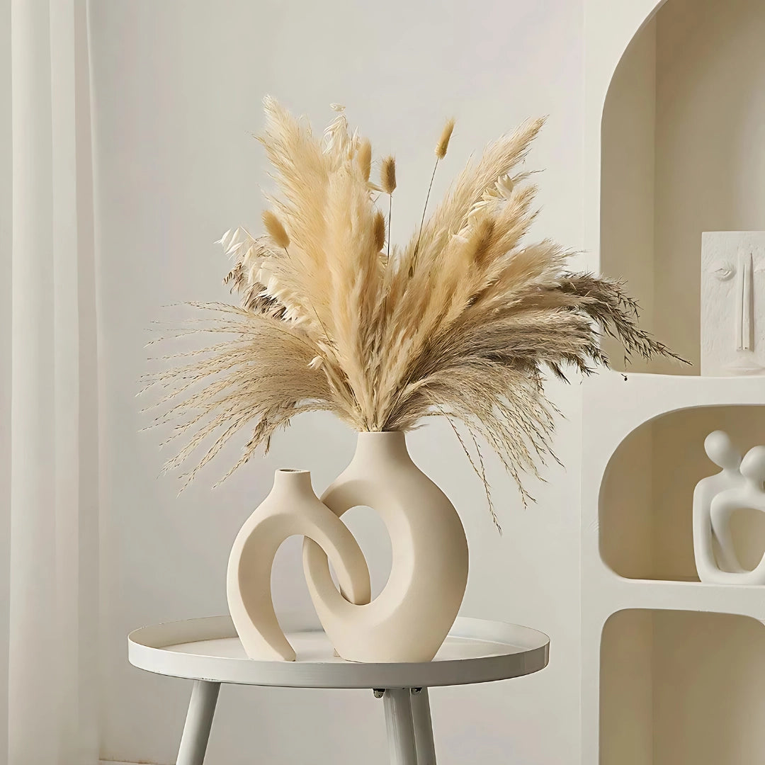 Modern abstract ceramic vase in beige color placed on a wooden surface, styled with twigs, in a well-lit room, embodying bohemian decor elements.