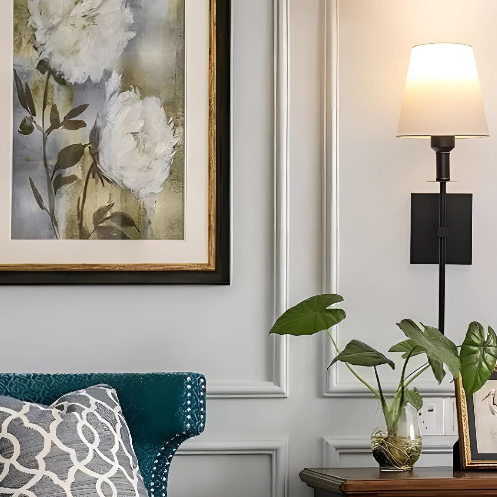 Modern black adjustable wall sconce mounted on a white wall, illuminating a minimalist interior space with a hint of yellow light. The room features green plants and a picture frame, enhancing the contemporary design.