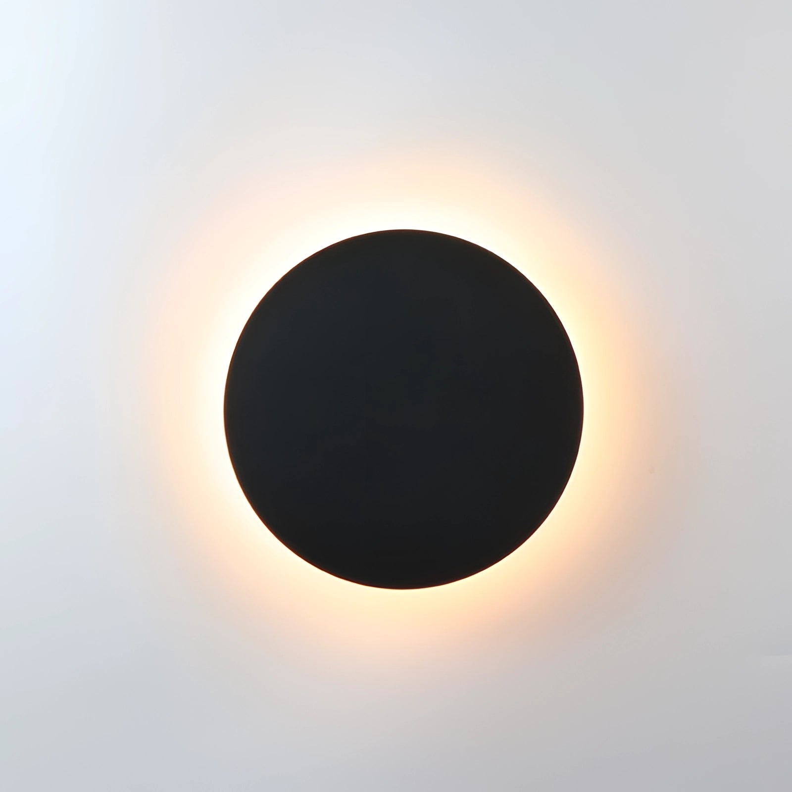 Modern black circular LED wall sconce with a minimalist design, emitting a halo glow resembling a celestial phenomenon like an eclipse or full moon.