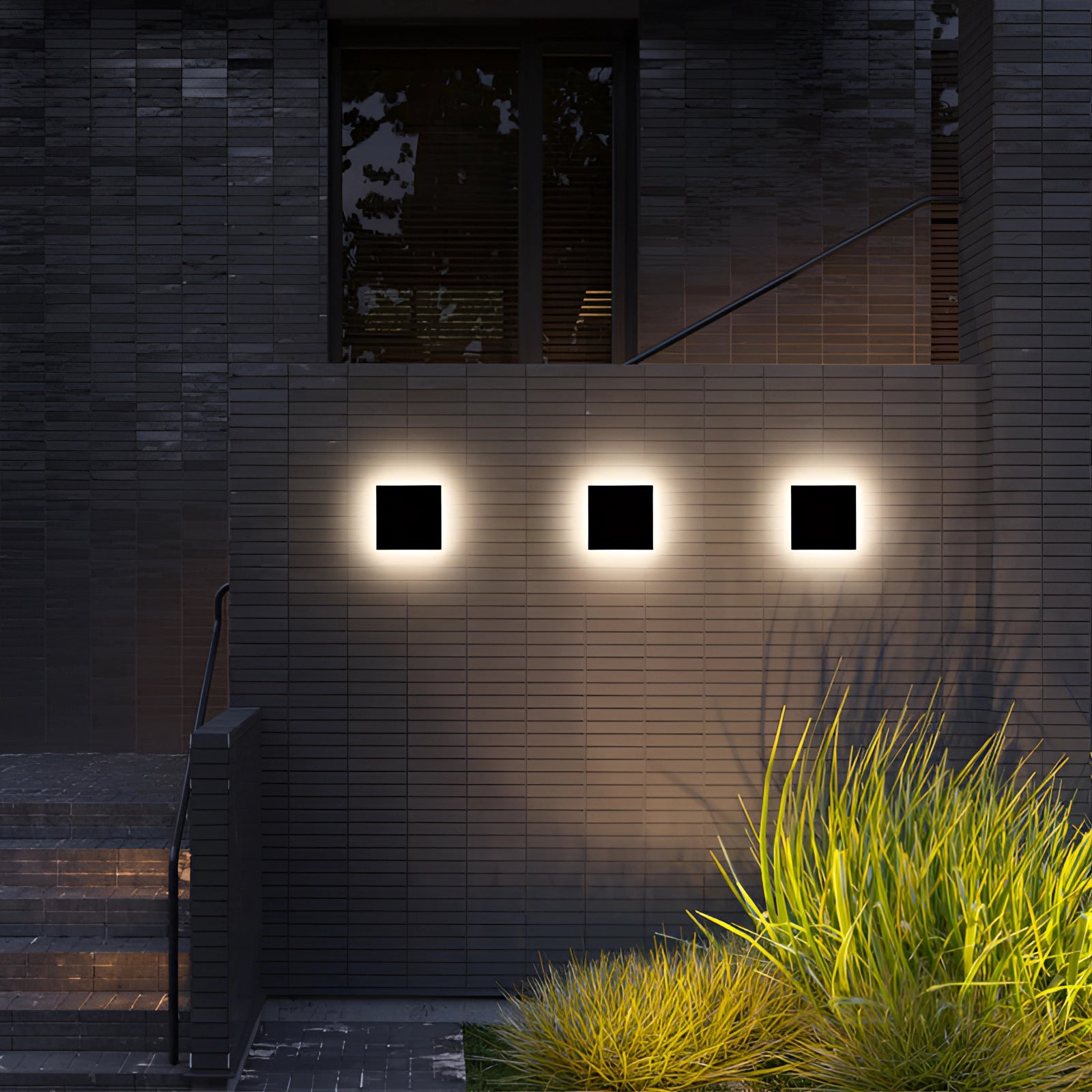 Modern black circular LED wall sconce mounted on an exterior brick wall, emitting a minimalist halo glow near a large window with a building facade and surrounding greenery.