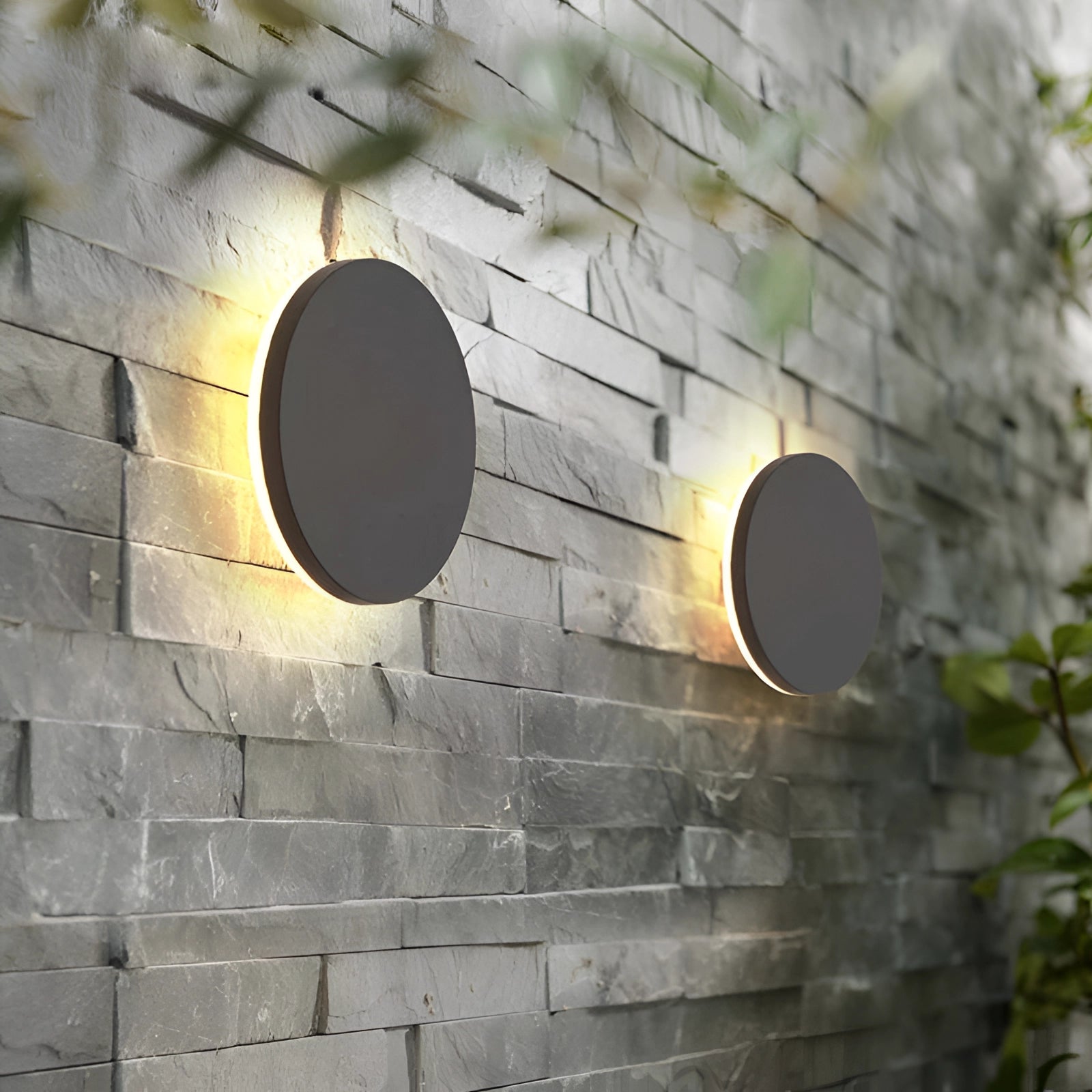 Modern black circular LED wall sconce mounted on a brick wall, emitting a minimalist halo glow, with wood and nature elements in the background.