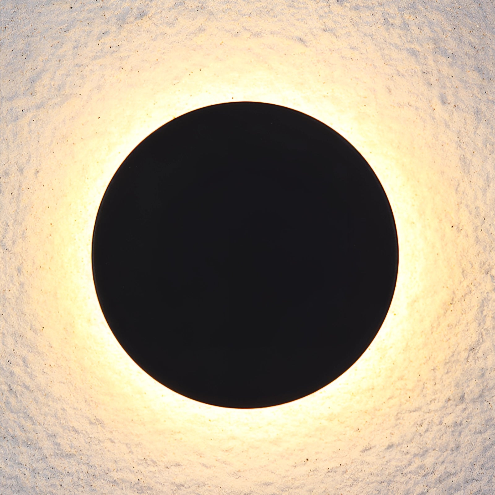 Modern black circular LED wall sconce emitting a soft halo glow, resembling a crescent moon in a minimalist design, set against a dark background.