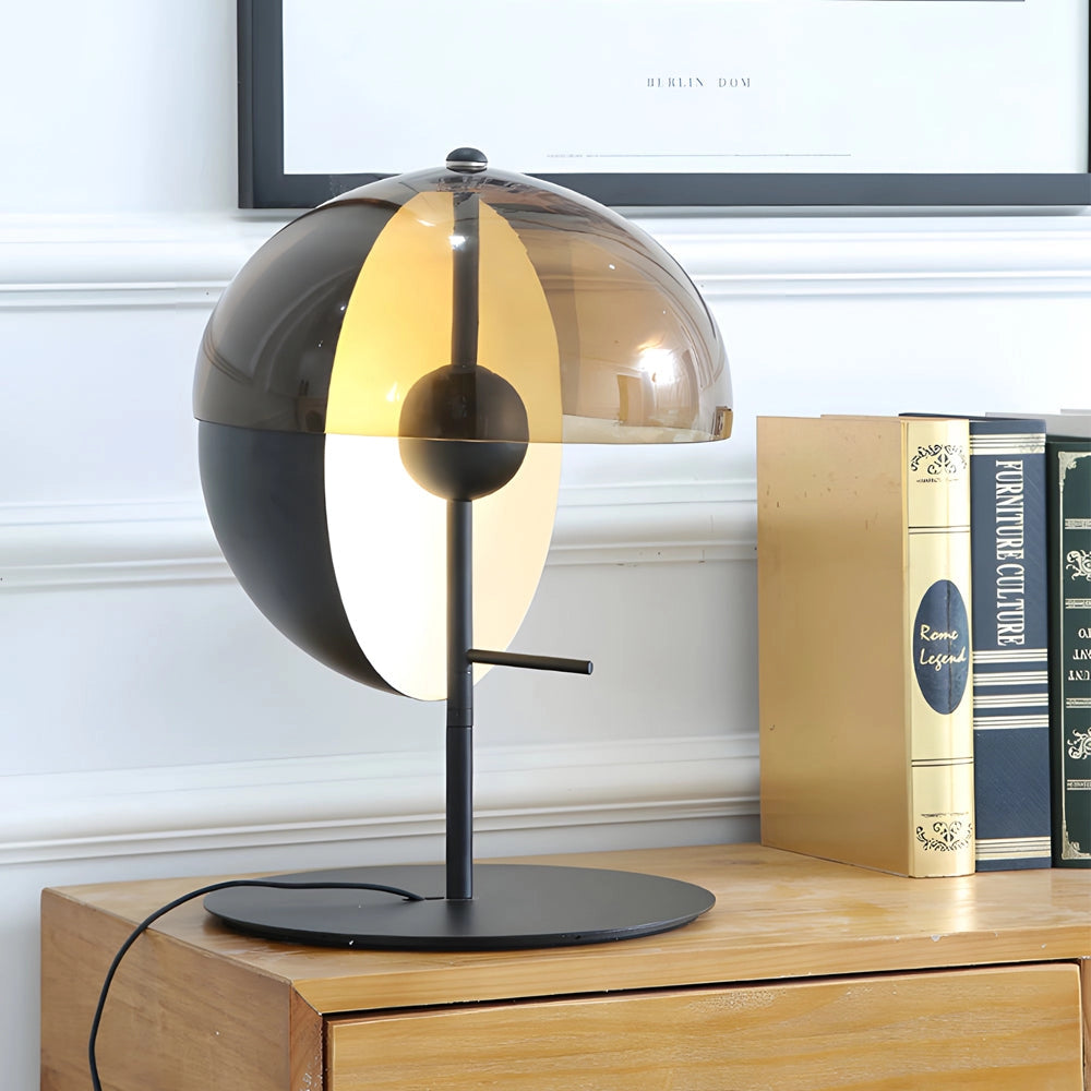 Modern black and gold half-sphere globe desk lamp on a wooden shelf, surrounded by books and electronic devices.