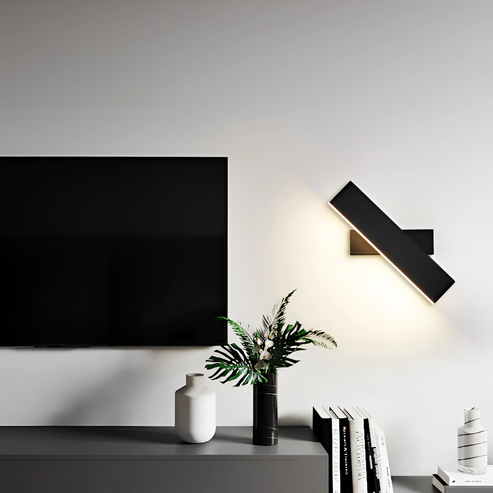 Modern black LED wall sconce with a minimalist geometric design, mounted on a grey wall next to a houseplant. The sconce emits a cold white light, enhancing the contemporary interior design.