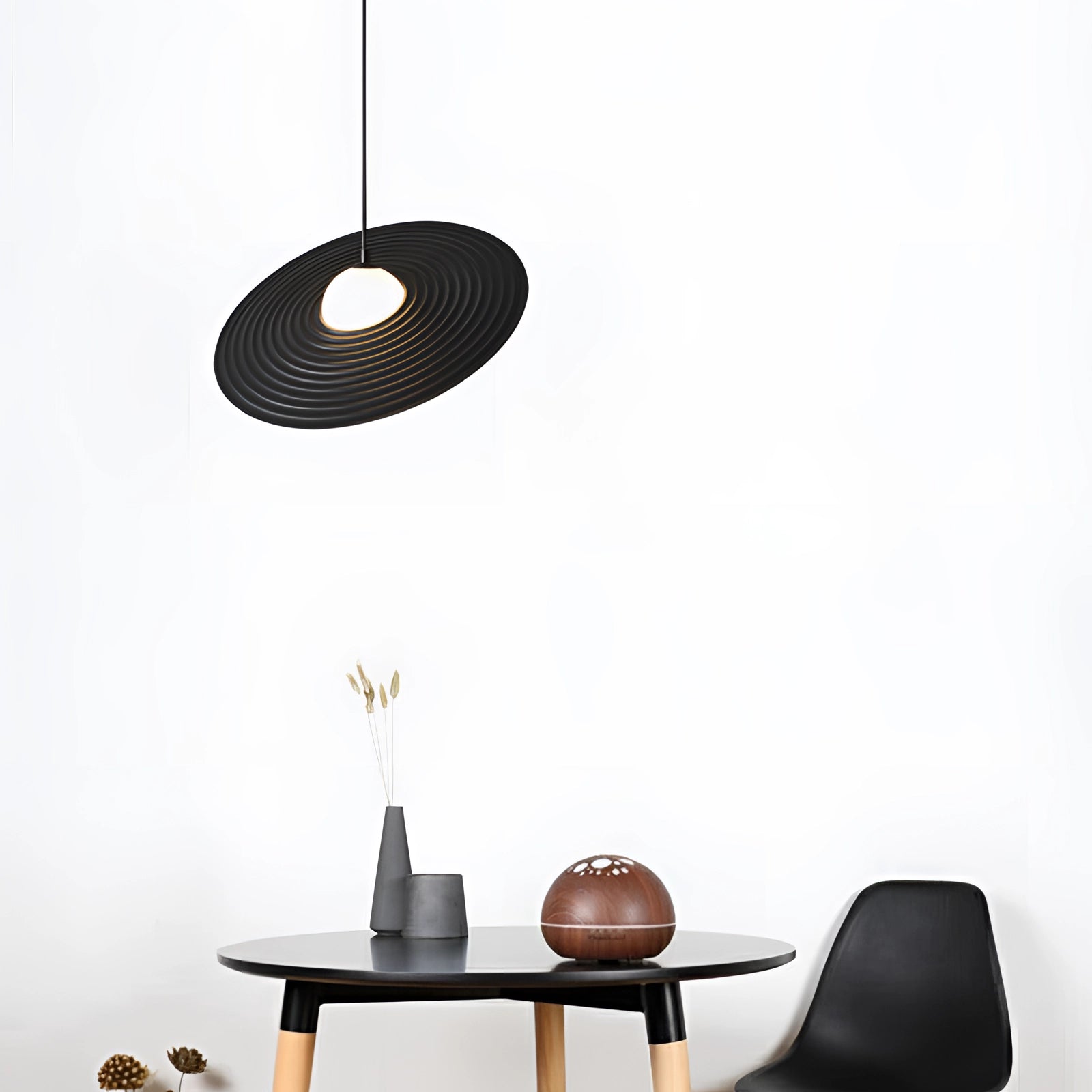 Modern black oval pendant light hanging above a wooden table, surrounded by contemporary minimalist decor, including a small plant, blending seamlessly into a stylish interior design setting.