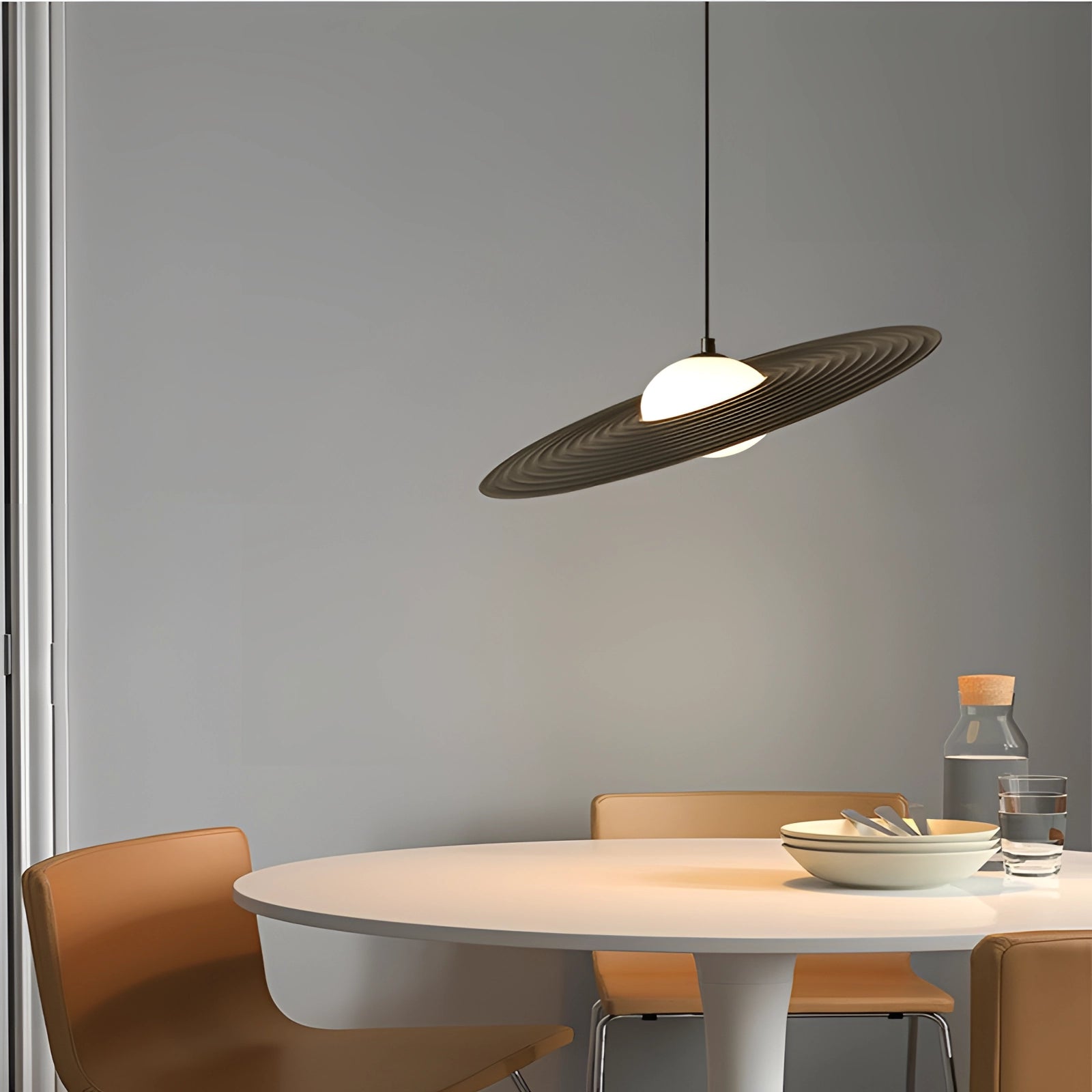 Modern black oval pendant light hanging in a minimalist interior setting, above a wooden table with shelving visible in the background.