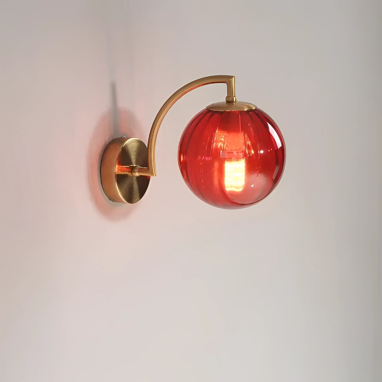 Modern brass globe wall sconce with a red finish, featuring a 22.7cm wide decorative lamp design. The sconce is mounted on a wall, showcasing a globe shape made of metal with a smooth, reflective surface. The fixture adds a stylish and contemporary touch to any room with its elegant and sophisticated design.