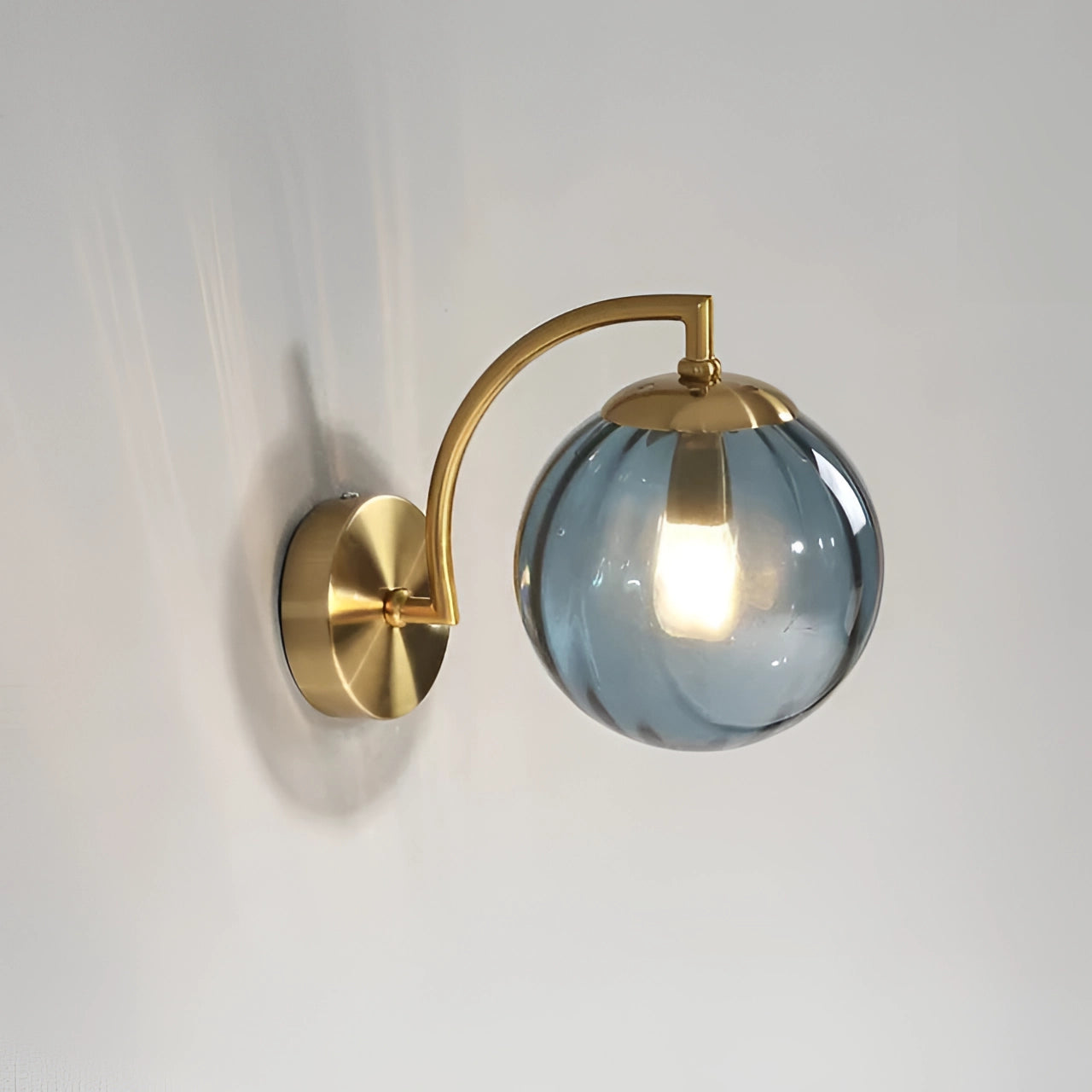 Modern brass globe wall sconce with a blue finish, featuring a circular design and decorative elements, mounted on a wooden background. The sconce is crafted from metal and serves as an elegant ornamental lamp for contemporary interiors.