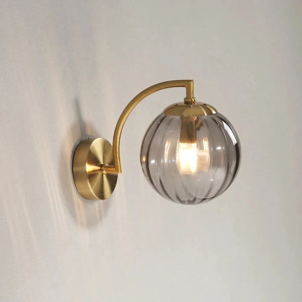 Modern brass globe wall sconce with an amber-tinted glass globe, 22.7cm wide, featuring a decorative gold metal fixture, mounted on a wood base.