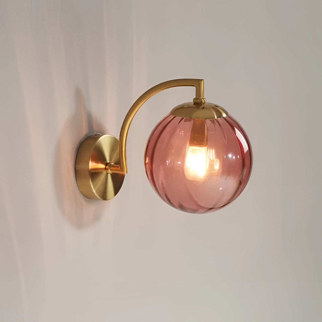 Modern brass globe wall sconce with a claret finish, featuring a decorative circular design and amber tint, mounted on a wooden base.