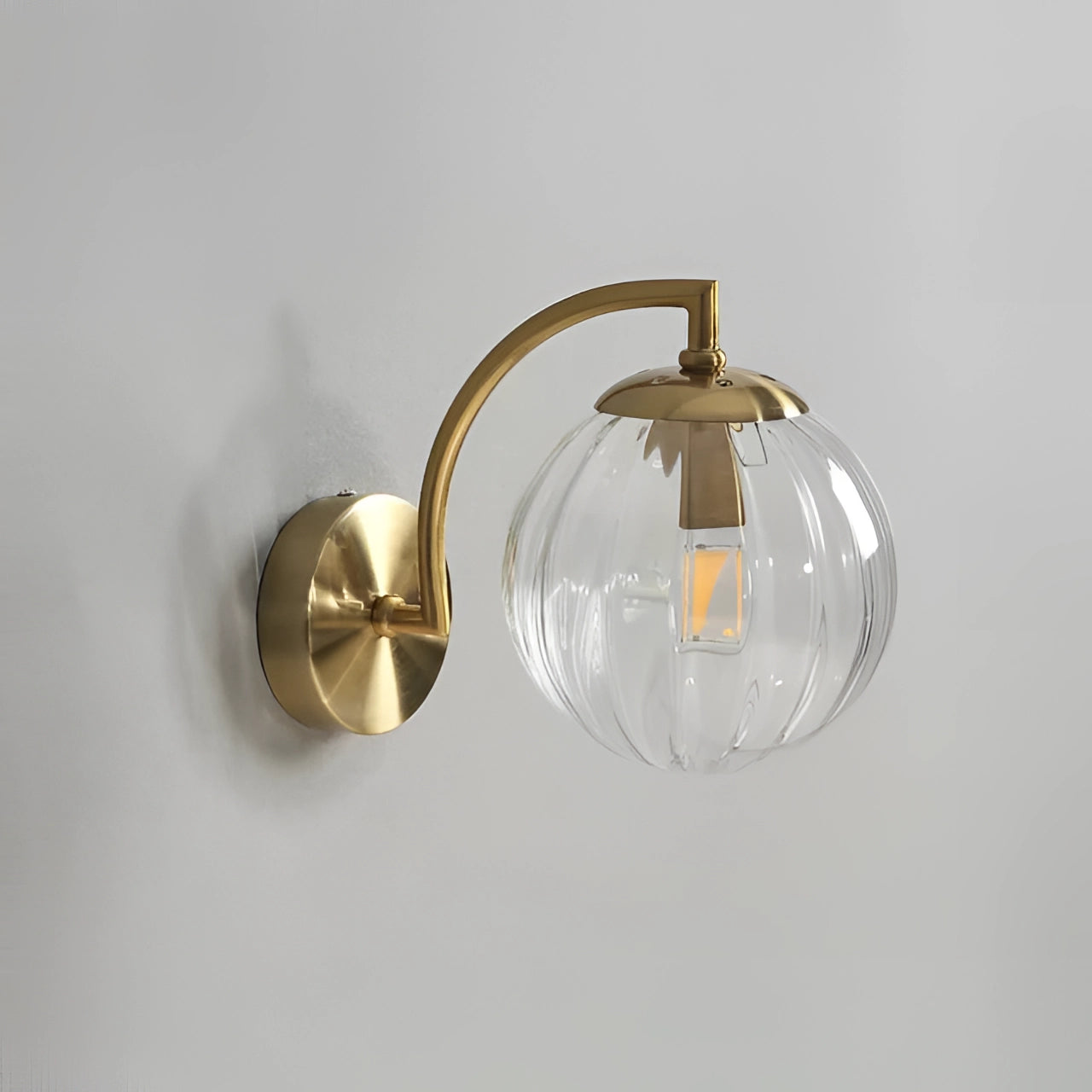 Modern brass globe wall sconce with a clear glass shade, measuring 22.7cm wide, featuring a decorative lamp design. The sconce has a circular shape with a metallic finish, suitable for wall mounting to provide ambient lighting.