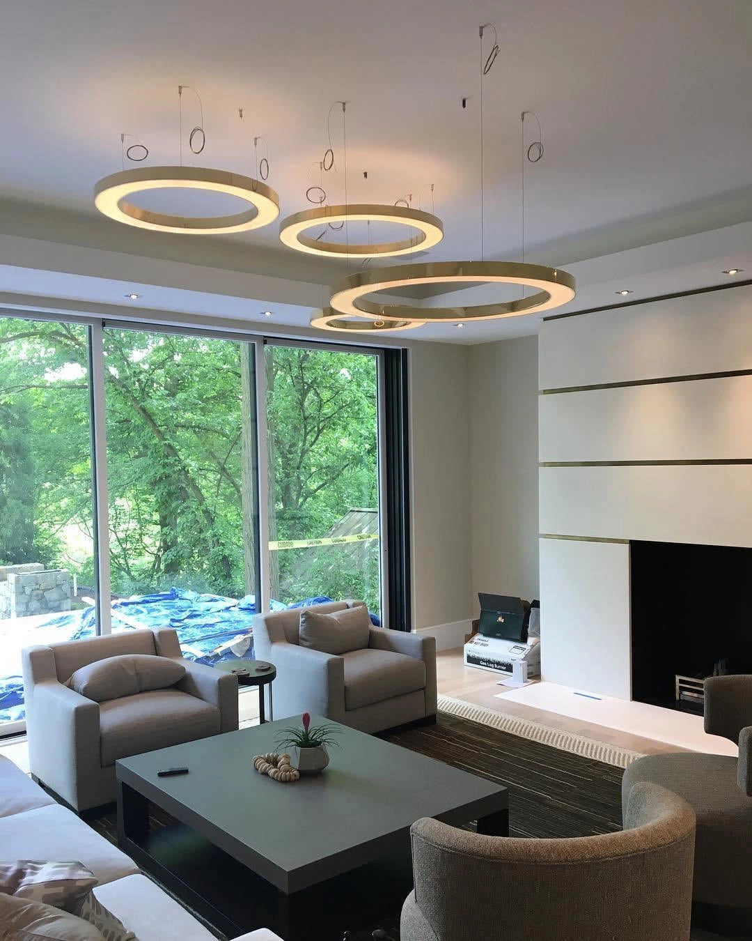 Modern circular LED ring pendant light illuminating a luxurious hotel lobby, featuring elegant furniture including tables, chairs, and couches with a focus on sophisticated interior design elements and warm wooden flooring.