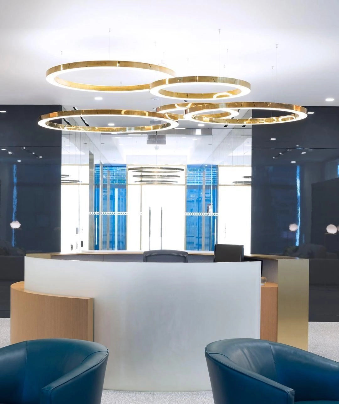 A modern circular LED ring pendant light hanging from the ceiling in a luxurious hotel lobby with blue accents, featuring elegant interior design elements like glass walls and stylish flooring.