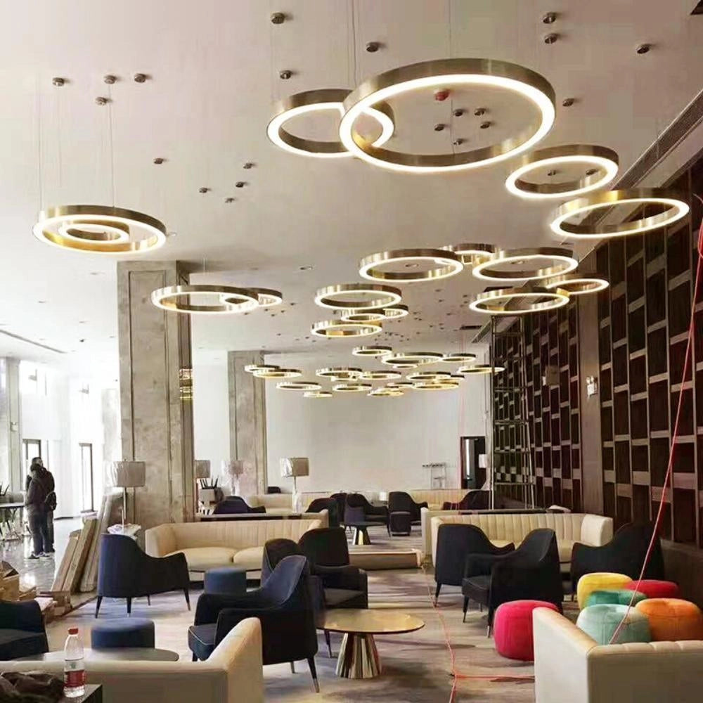 A stylish modern circular LED ring pendant light hanging in a luxury hotel lobby, complementing the sleek interior design featuring contemporary furniture, including chairs and tables, and sophisticated architectural elements such as polished floors and elegant walls.