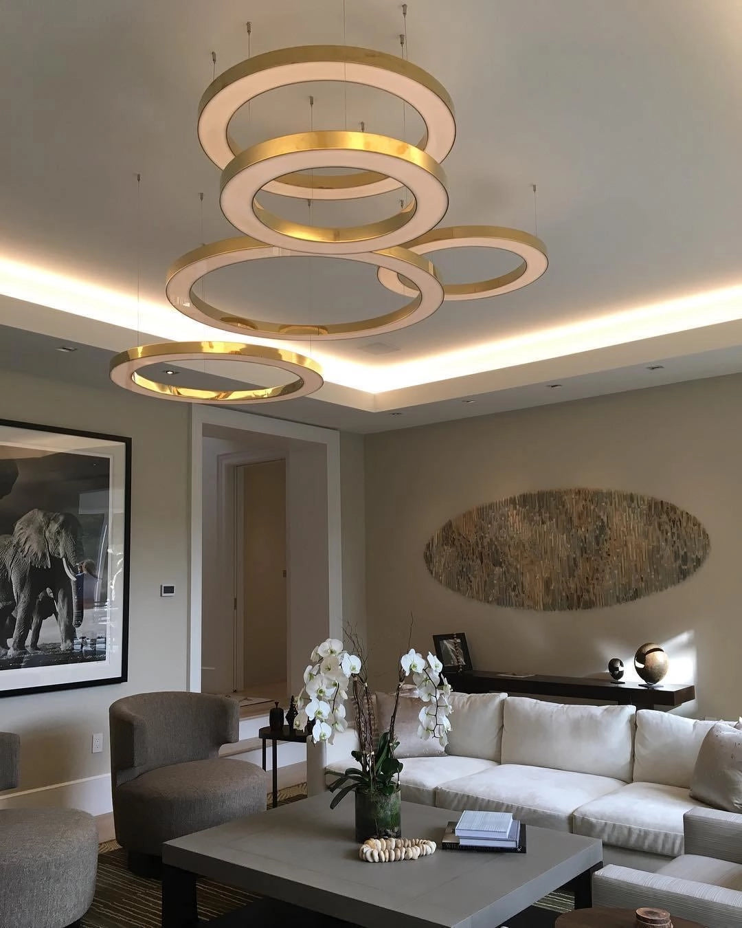 Modern circular LED ring pendant light hanging in a luxurious hotel lobby setting, featuring elegant interior design elements such as a plush couch, stylish table, decorative plant, and framed artwork, all contributing to a sophisticated living room ambiance.