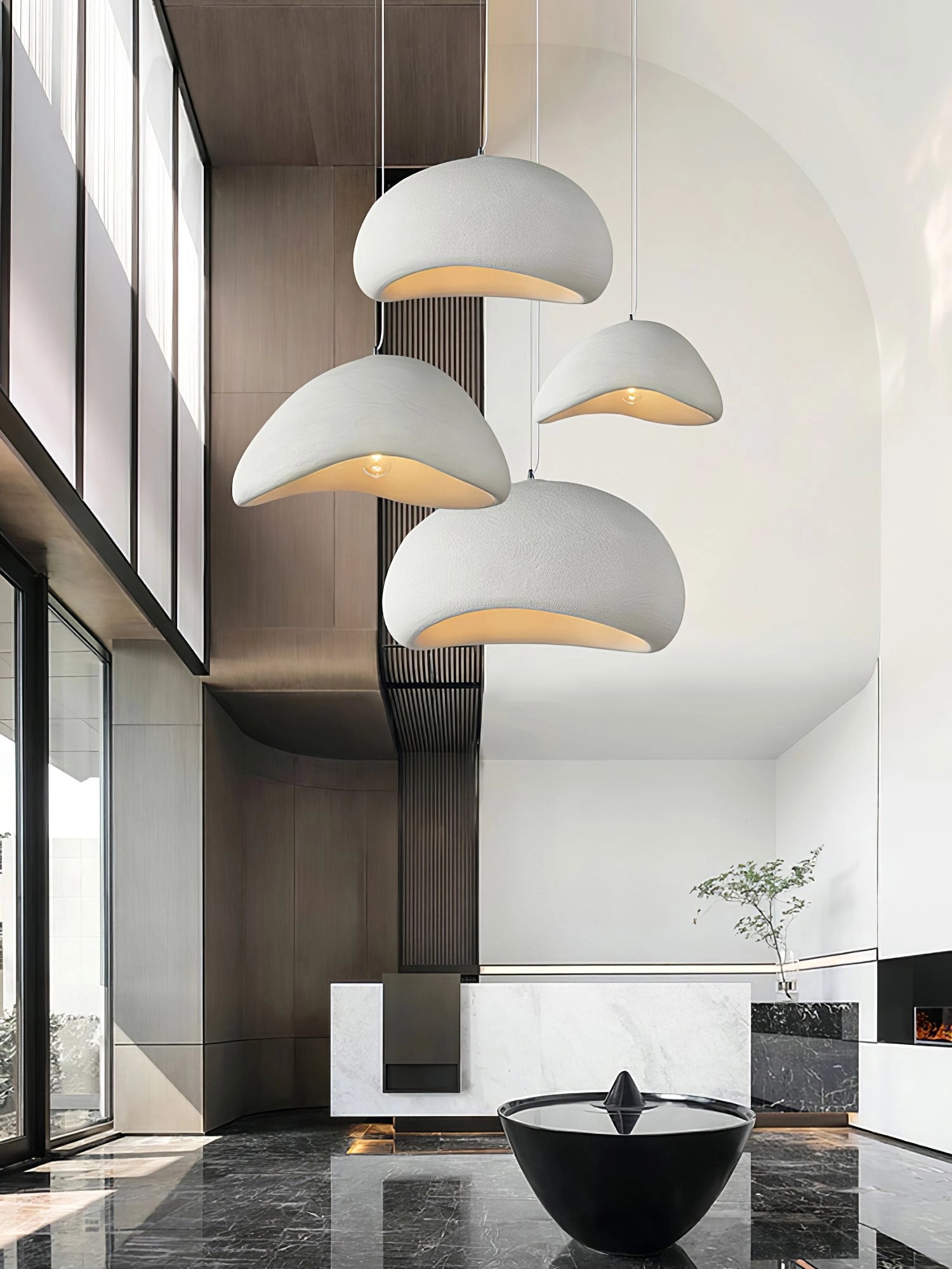 Modern curved pendant light with a minimalist sculptural design in white, hanging in an interior setting with architectural elements and subtle plant decoration.