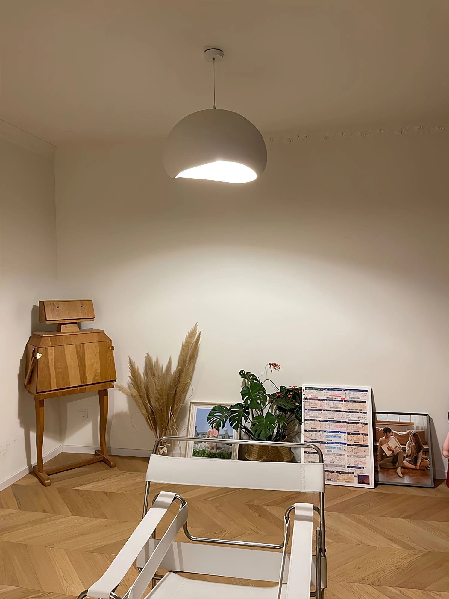 A modern curved pendant light with a minimalist sculptural design hanging above a wooden table, surrounded by an aesthetically pleasing interior that includes hardwood flooring and a green plant, creating a comfortable and stylish atmosphere.