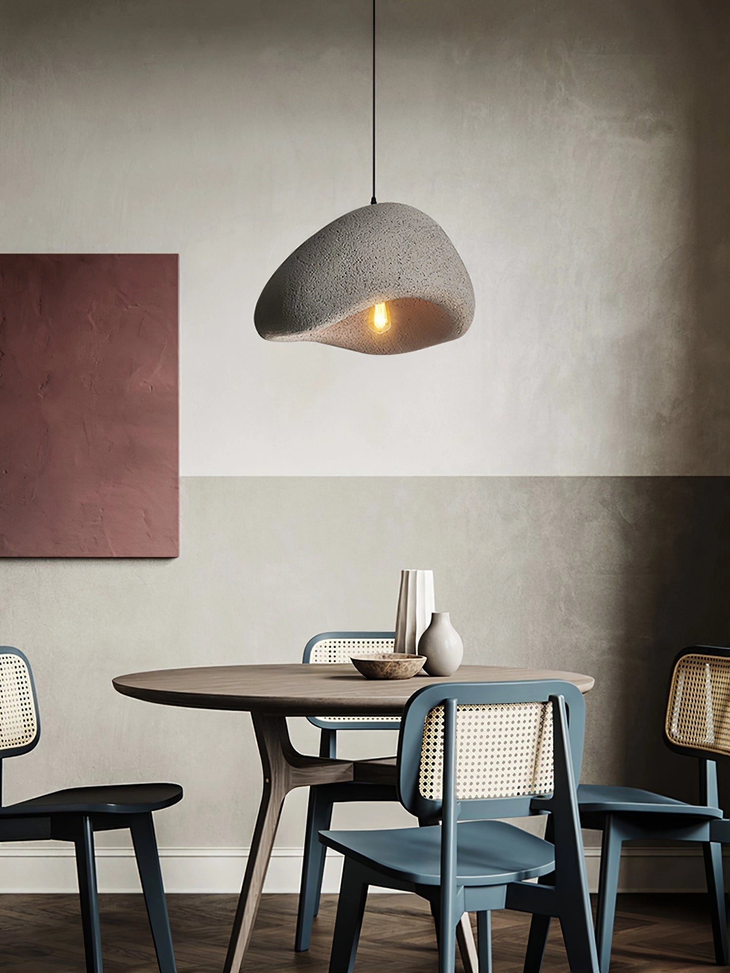 A minimalist sculptural pendant light with a modern curved design, featured in a gray finish, hanging above a contemporary wooden dining table and chairs in a stylishly designed interior space. The light measures 60cm in diameter and 35cm in height.