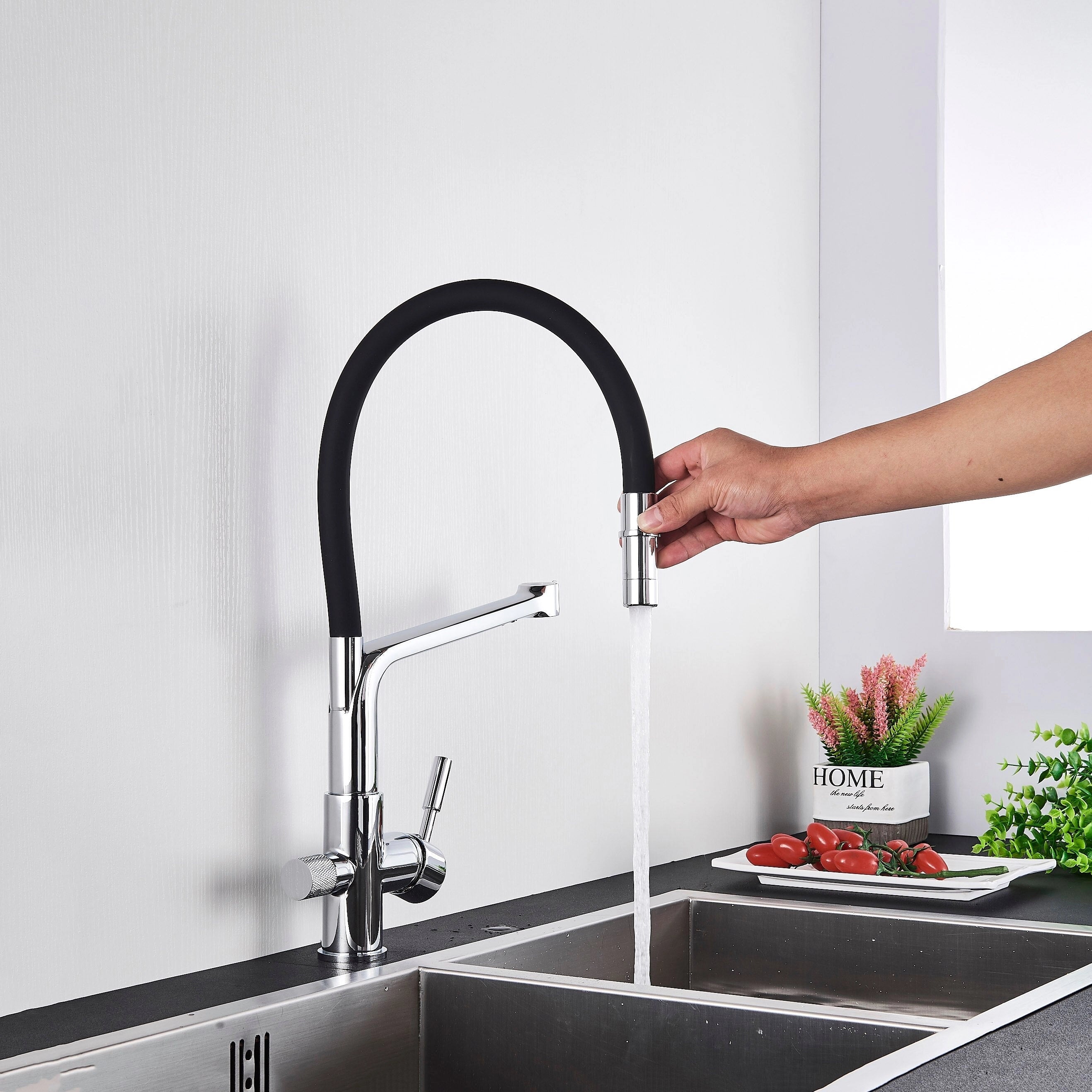 Modern dual-function black and chrome pull-down kitchen faucet installed over a kitchen sink, with a plant in a flowerpot nearby.