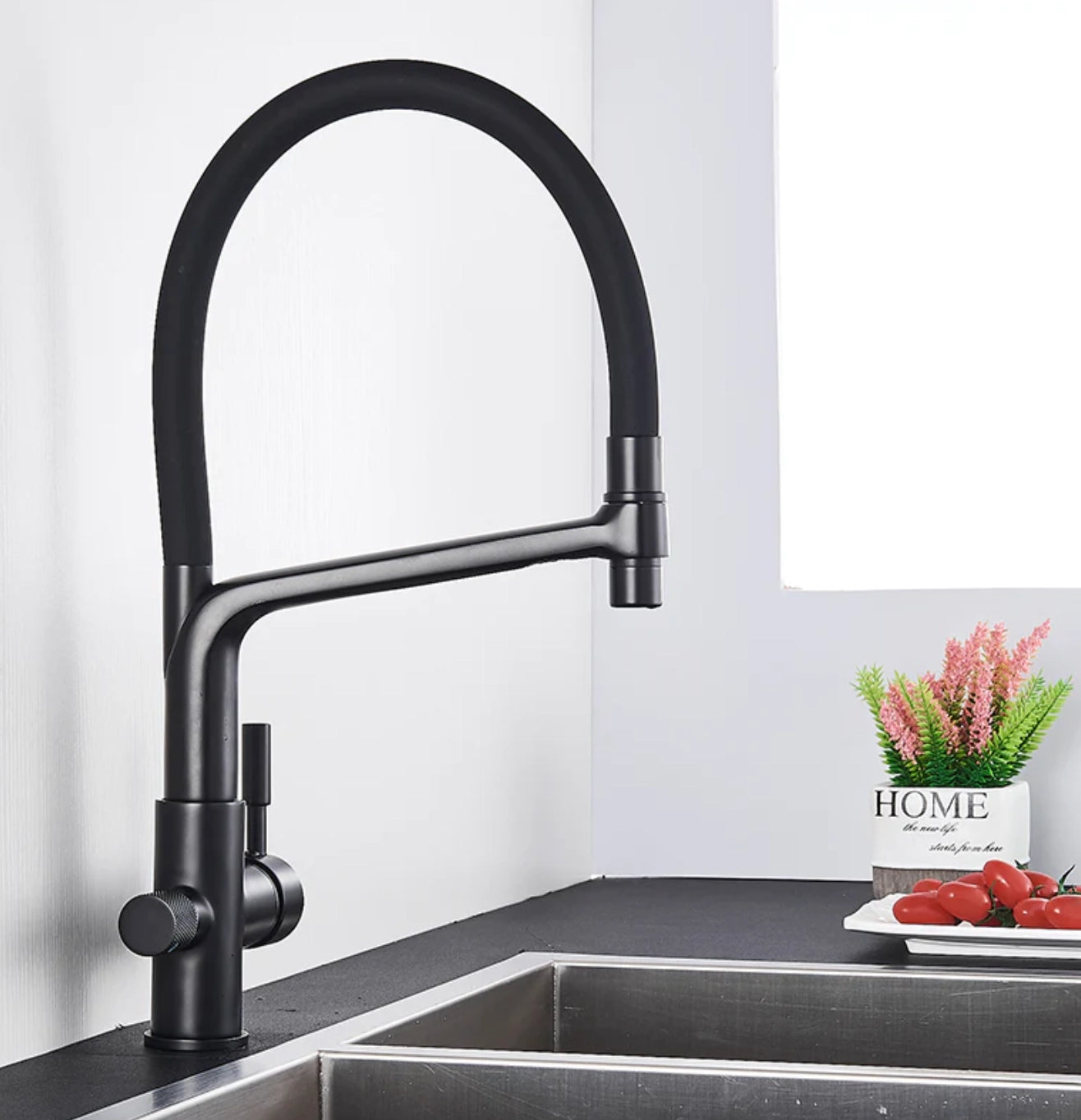 Sleek modern dual-function black and chrome pull-down kitchen faucet installed above a rectangular kitchen sink on a countertop, with a plant in the background.