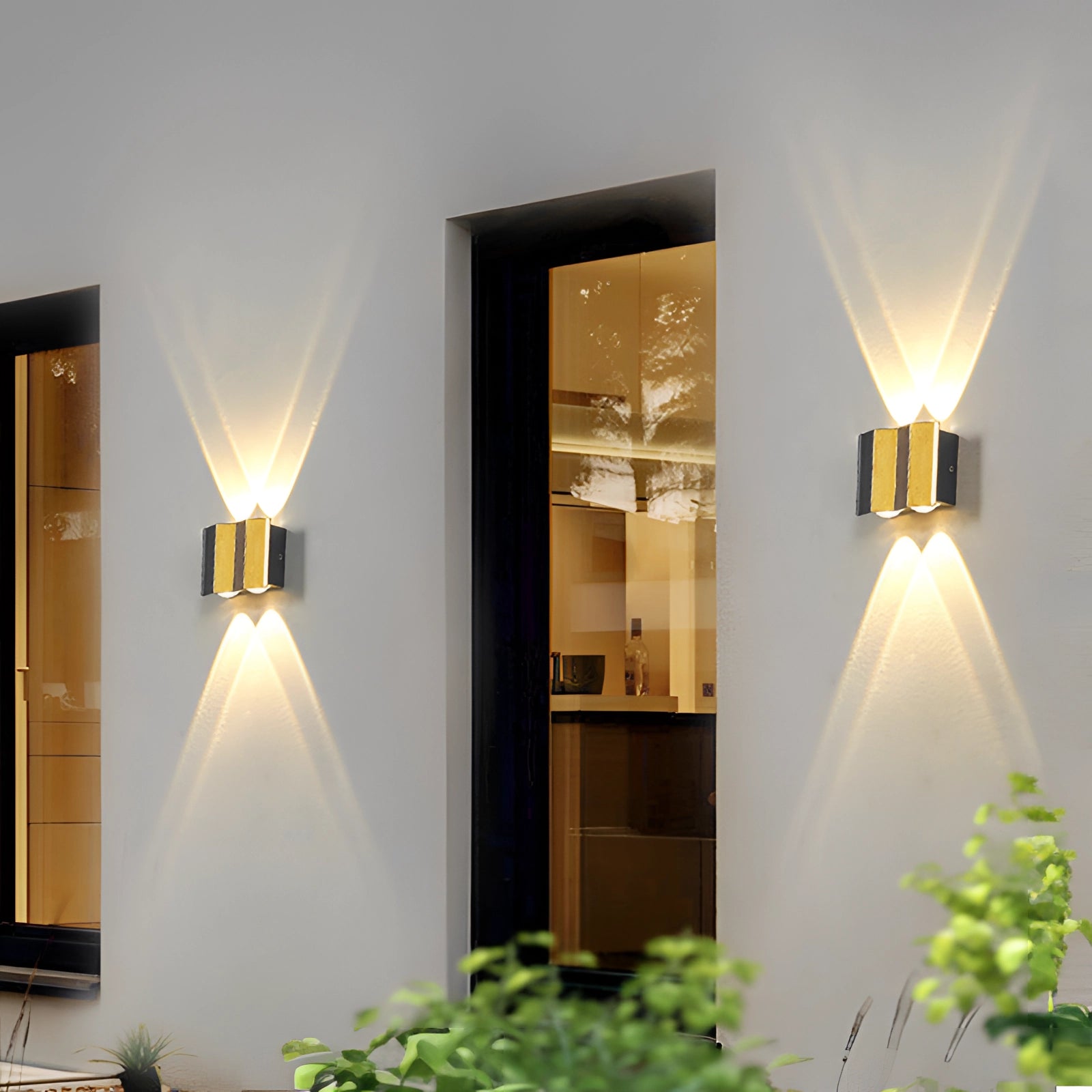 Modern geometric LED wall lamp mounted on an exterior wall, emitting a bright white light (5000K) at night. The lamp's sleek design features a waterproof outdoor fixture, suitable for Great Britain and Australia, enhancing the architectural aesthetic of the outdoor space. The lamp illuminates a surrounding area that includes natural elements like plants and wood accents.