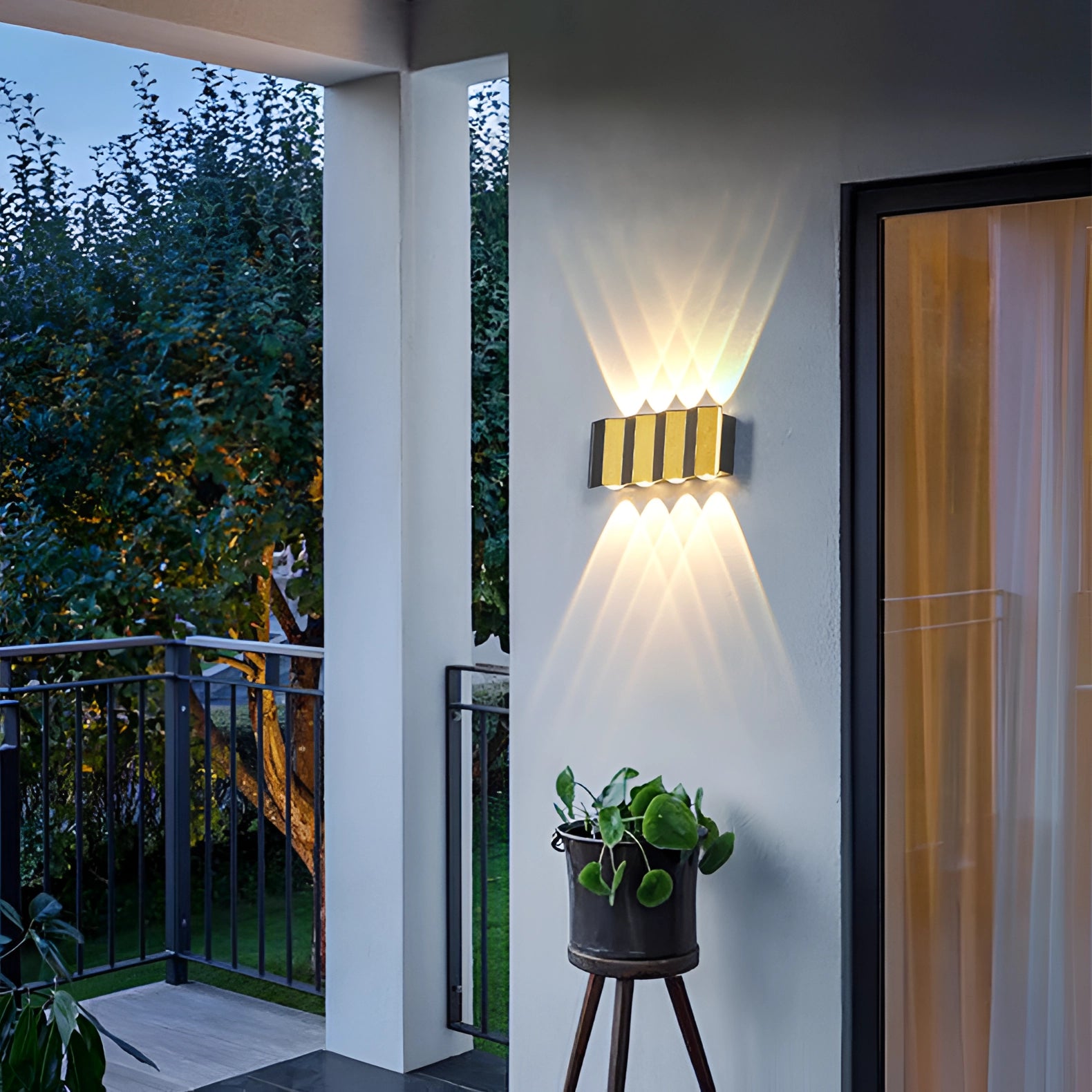 Modern geometric LED wall lamp mounted on an exterior wall, emitting a bright white light (5000K). The lamp features a sleek design suitable for Great Britain or Australia with voltage compatibility of 220-240 V. The background includes elements such as curtains and plants, suggesting an elegant outdoor setting.