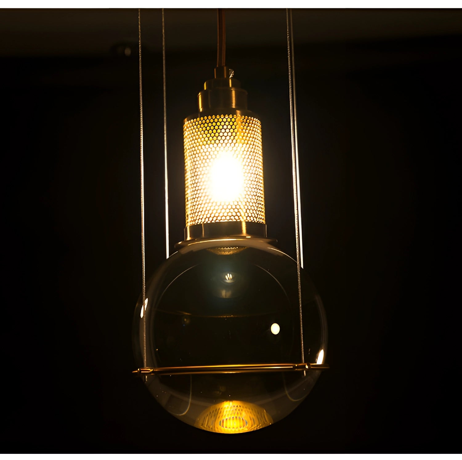 Modern glass globe pendant light with a gold finish, featuring minimalist designer lighting and an amber tint.