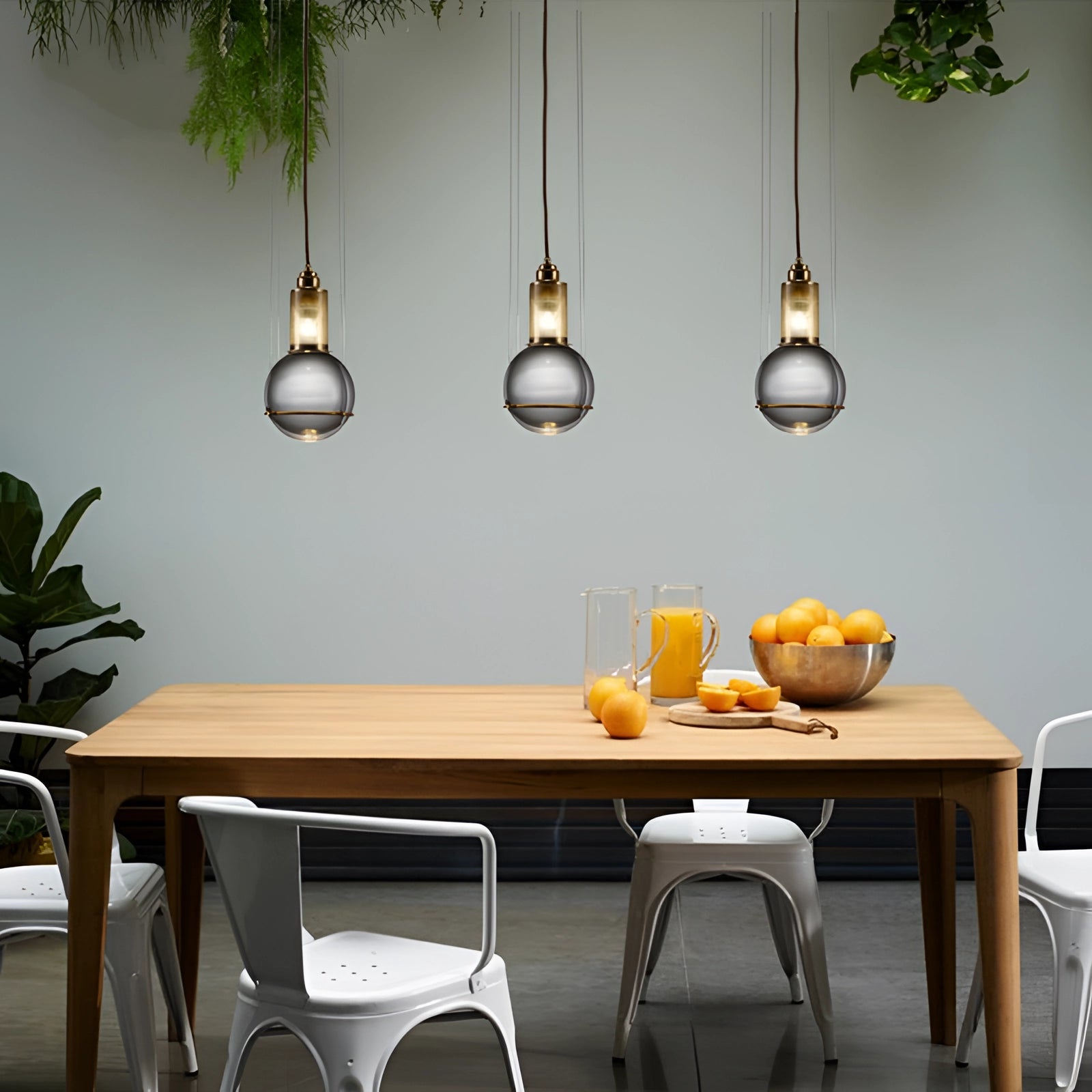 A modern glass globe pendant light with a gold finish hanging above a wooden table, surrounded by a stylish interior with minimalistic furniture and a touch of greenery from a nearby plant.