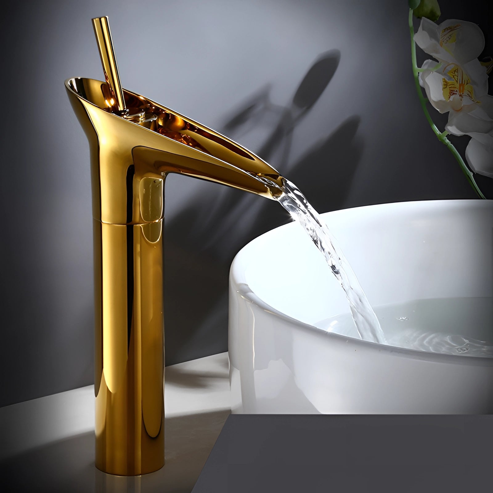 
Modern gold waterfall faucet made of luxury brass, designed for vessel sinks, displayed against a backdrop with decorative elements like a book and a cup.