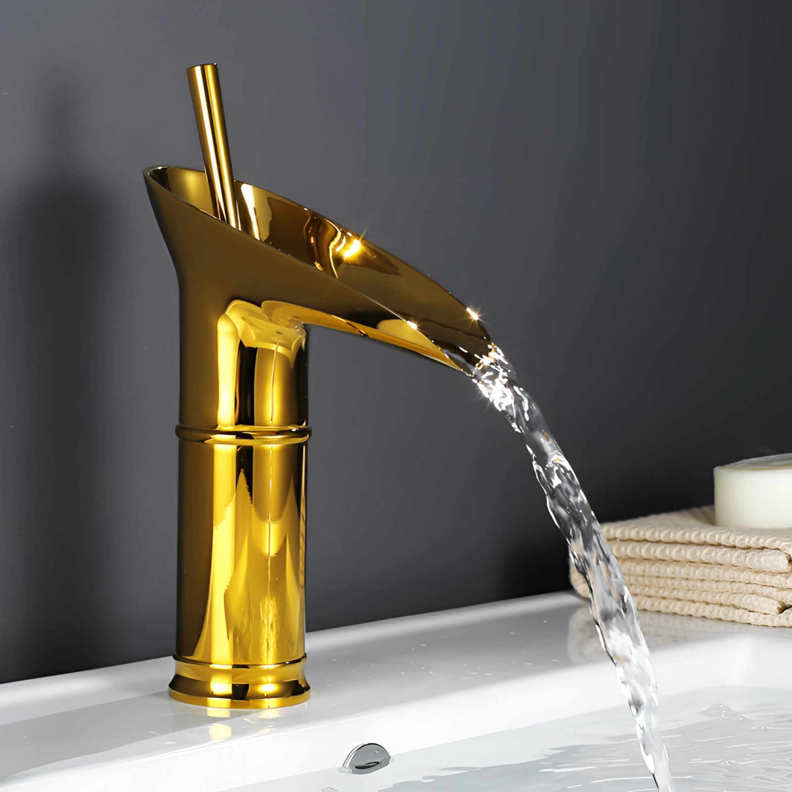 Modern gold waterfall faucet with a sleek design, featuring a luxurious brass finish, installed on a small vessel sink. Water elegantly cascades from the spout, creating a fluid and visually striking effect.