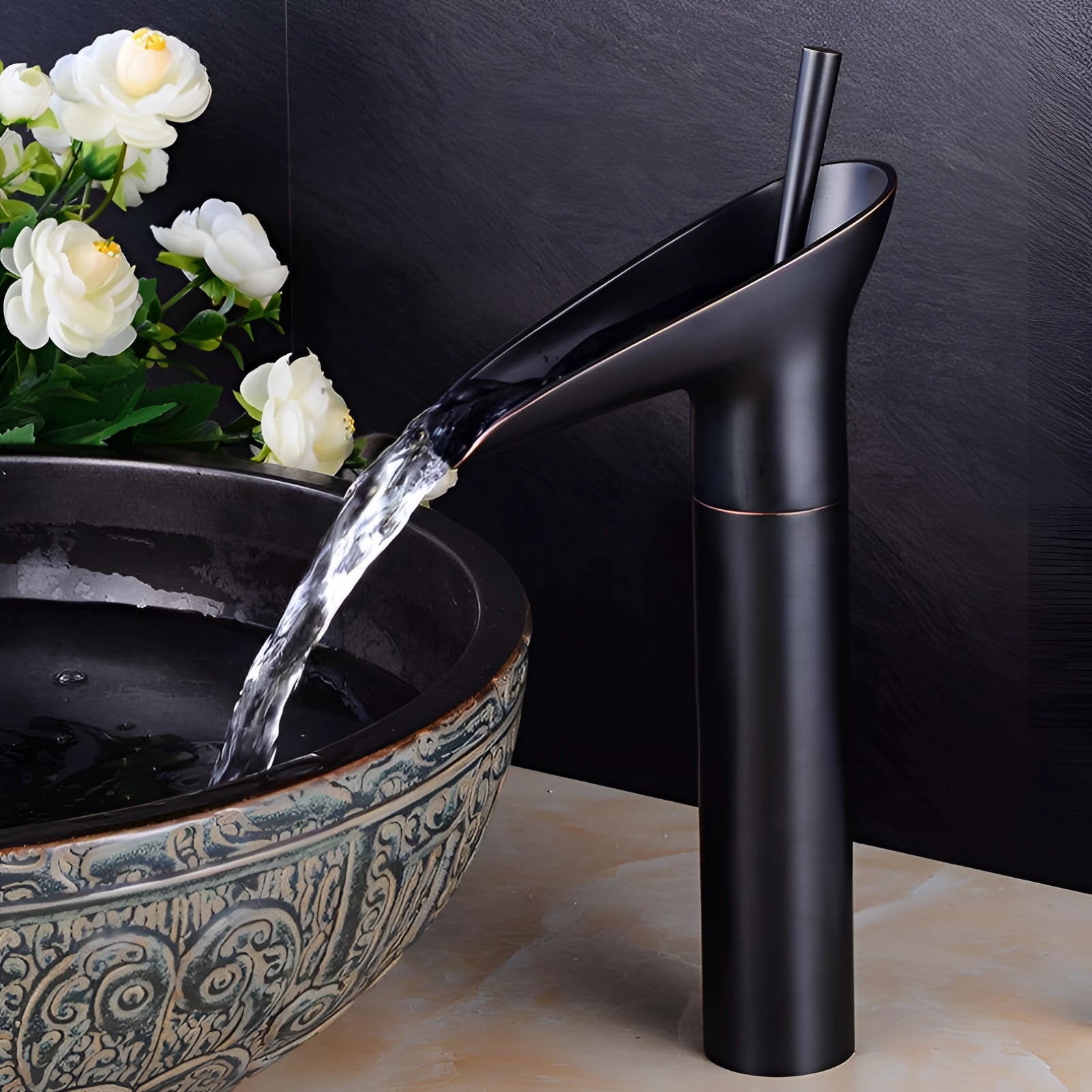 Black and gold modern waterfall faucet installed on a luxurious brass vessel sink, surrounded by elegant tableware and floral decor.