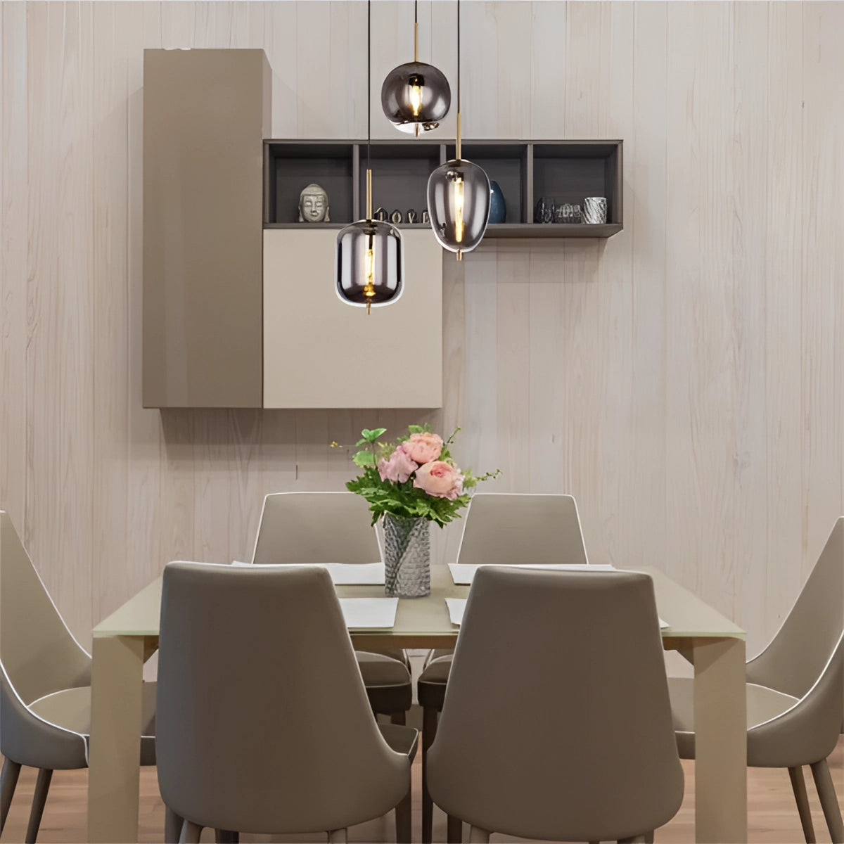 Modern Industrial Glass Pendant Lights with bronze finish hanging above a wooden dining table with white chairs, surrounded by contemporary interior design elements including a plant and grey flooring.