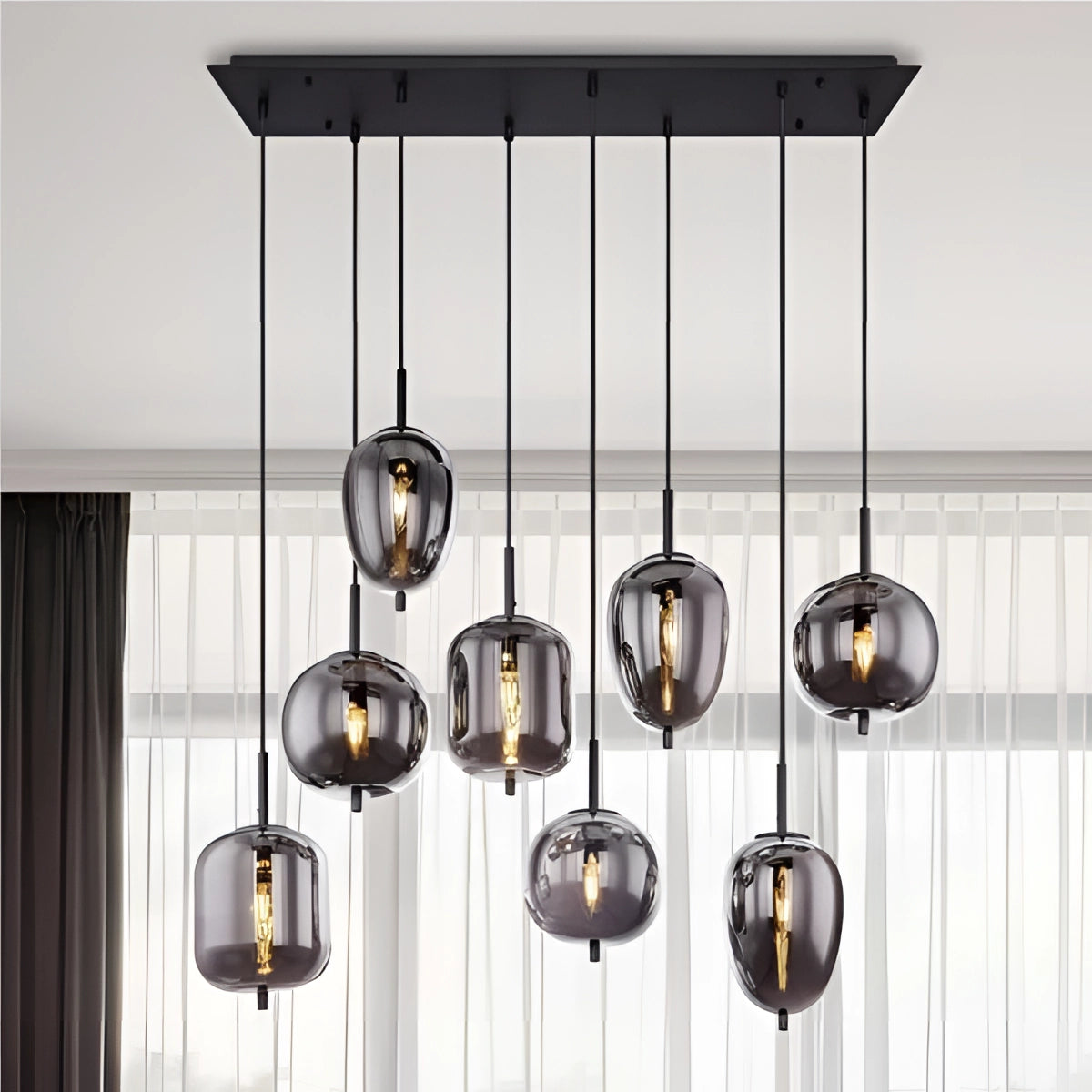 Modern industrial glass pendant lights with bronze finish hanging in dining room, featuring wooden shelves, curtains, and large windows in the background.