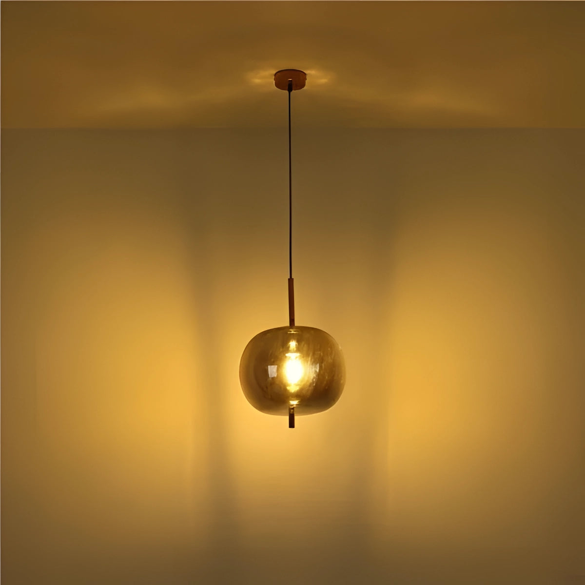 Modern industrial glass pendant light with bronze finish hanging from ceiling, illuminating a dining room with a warm glow; features circular glass shade and visible light bulb elements.